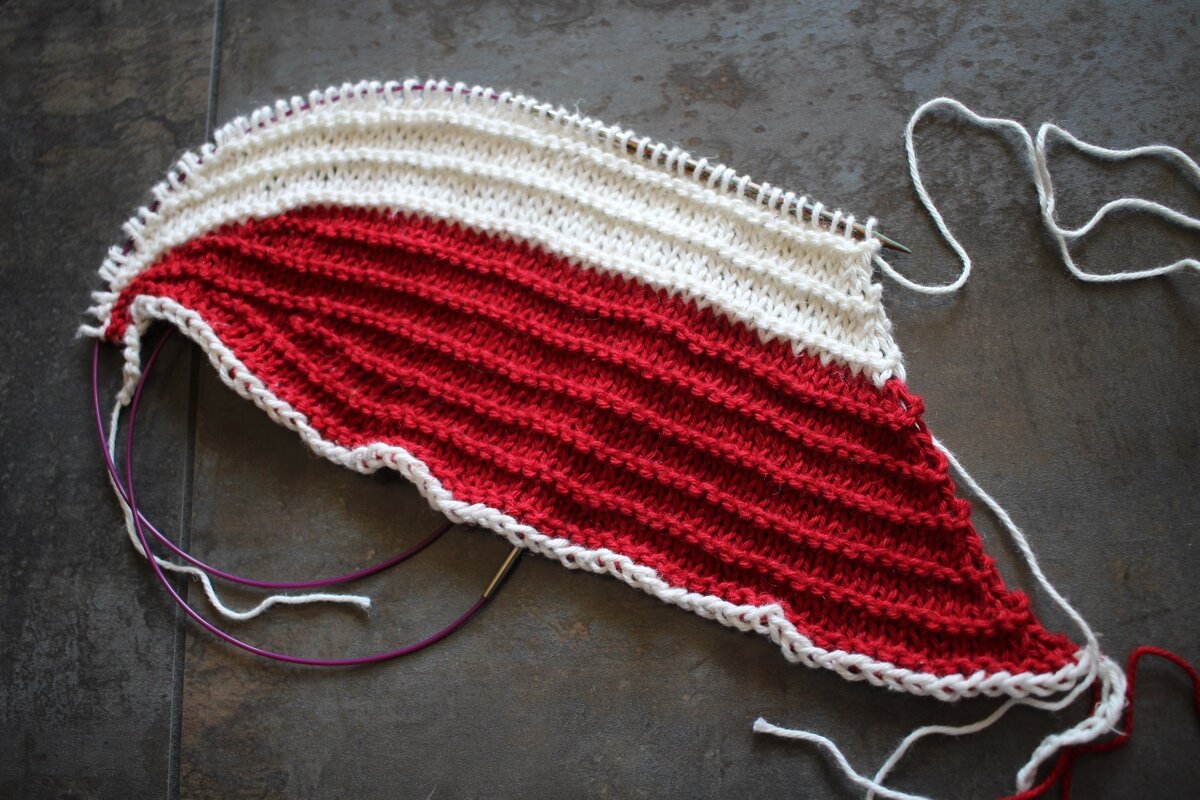 A partially knit hat in red and white with short row crown shaping and a provisional cast on. Sideways Swatching || withwool.com #knitswatch #darkmatterknits