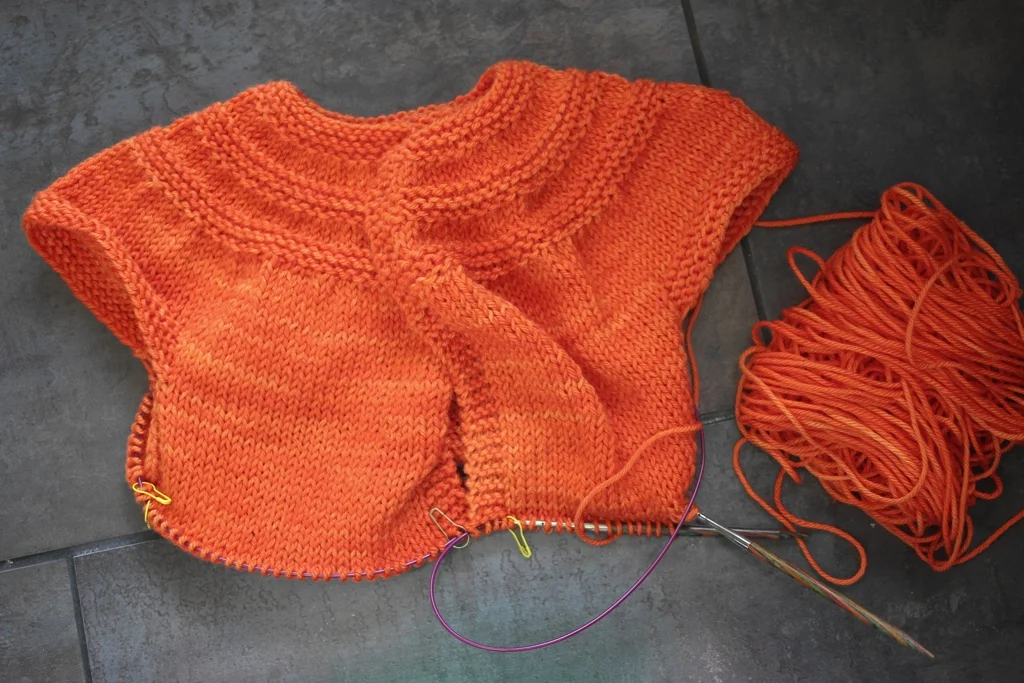A half-finished sweater for a toddler sitting next to a ball of yarn. Around Here || withwool.com