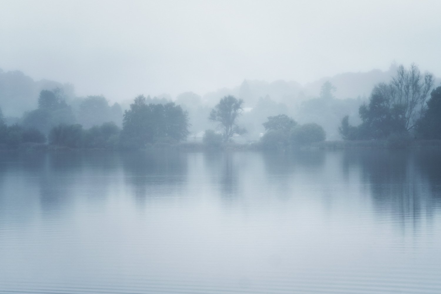 Misty Grasmere lake and distant trees viewed across open water
