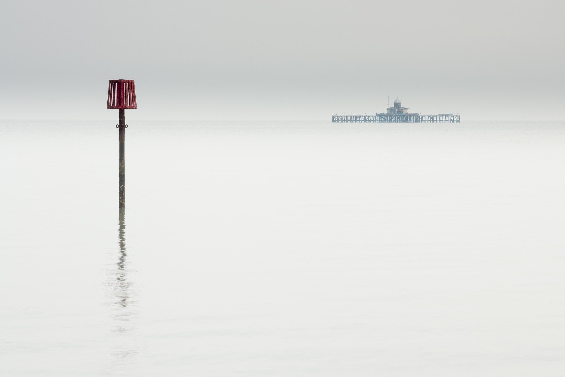 Navigation marker and distant remains of the old pier across quiet open water