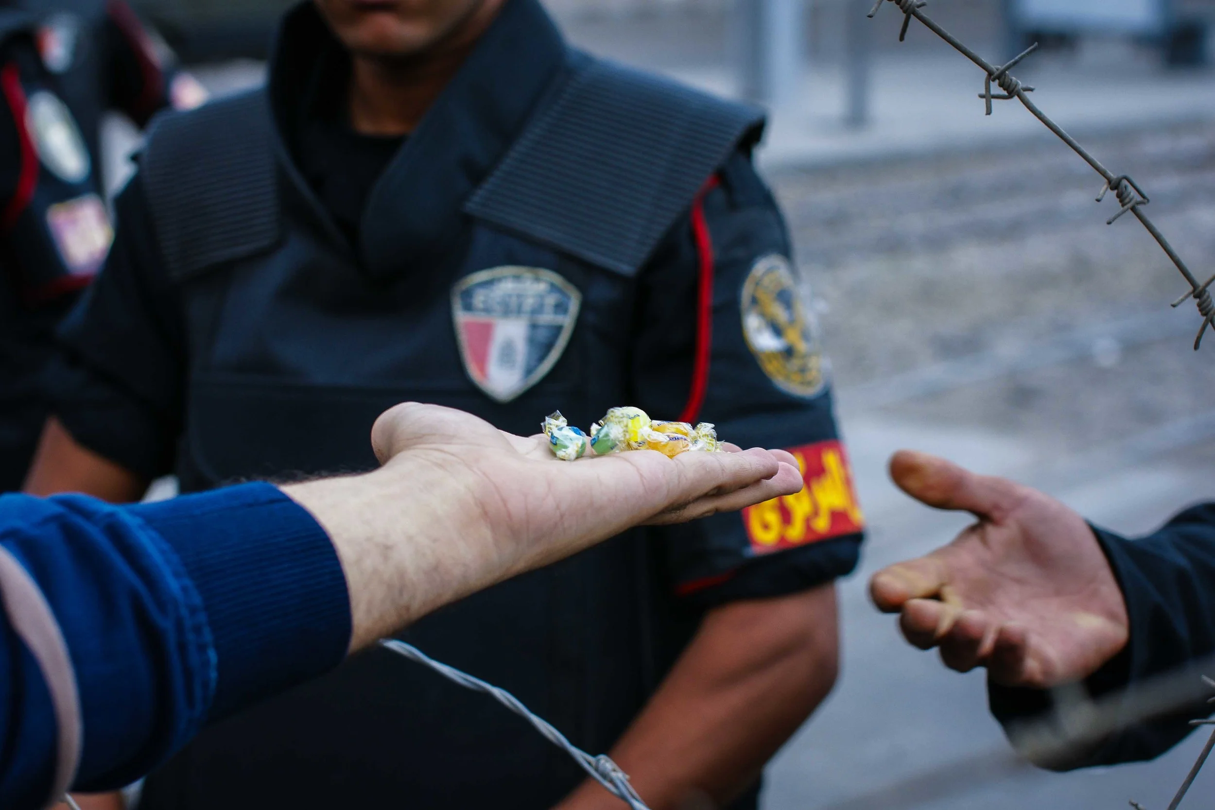 A protestor hands small candies through the barbed wire to a riot police officer. Candies, I might add, which the officer readily accepted.