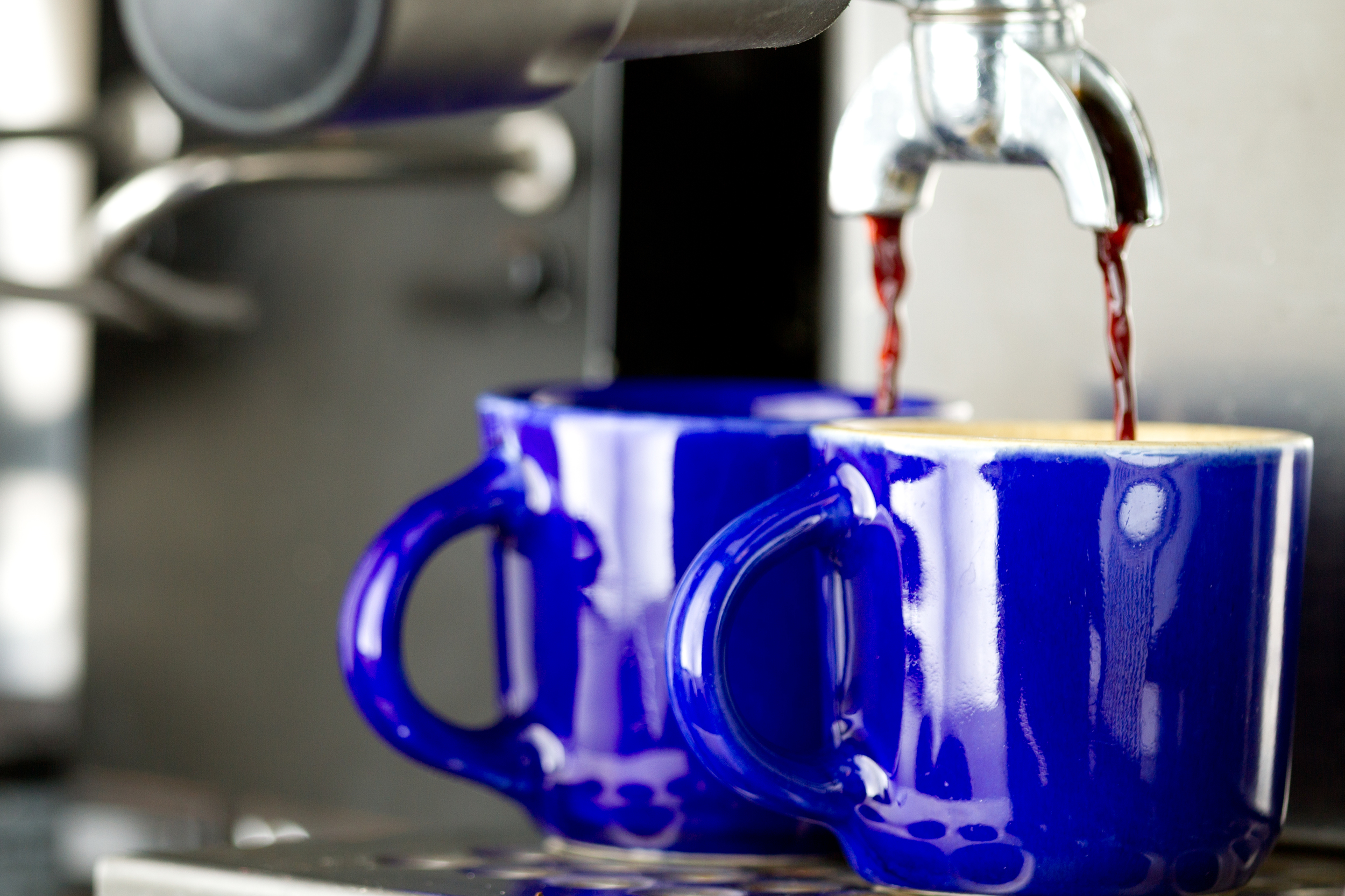 Professional food photo of coffee being brewing from a expresso machine on blue cups. Commercial photography