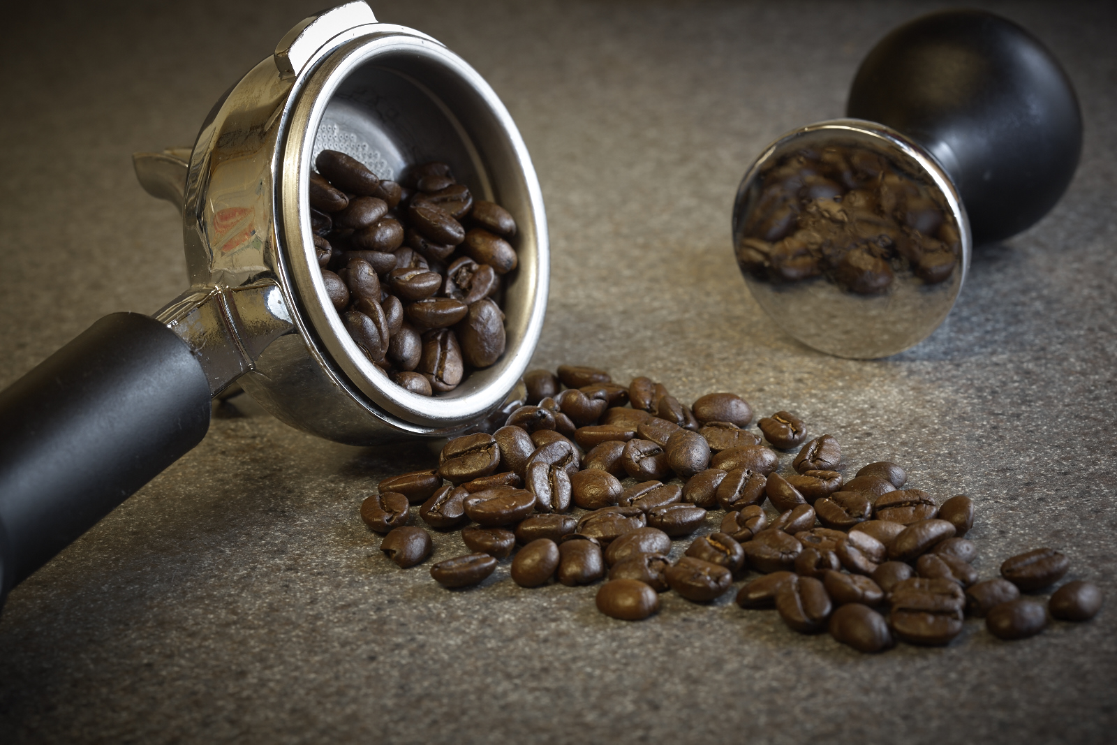 Professional food photo of coffee beans spilling from a expresso machine portafilter. Commercial photography