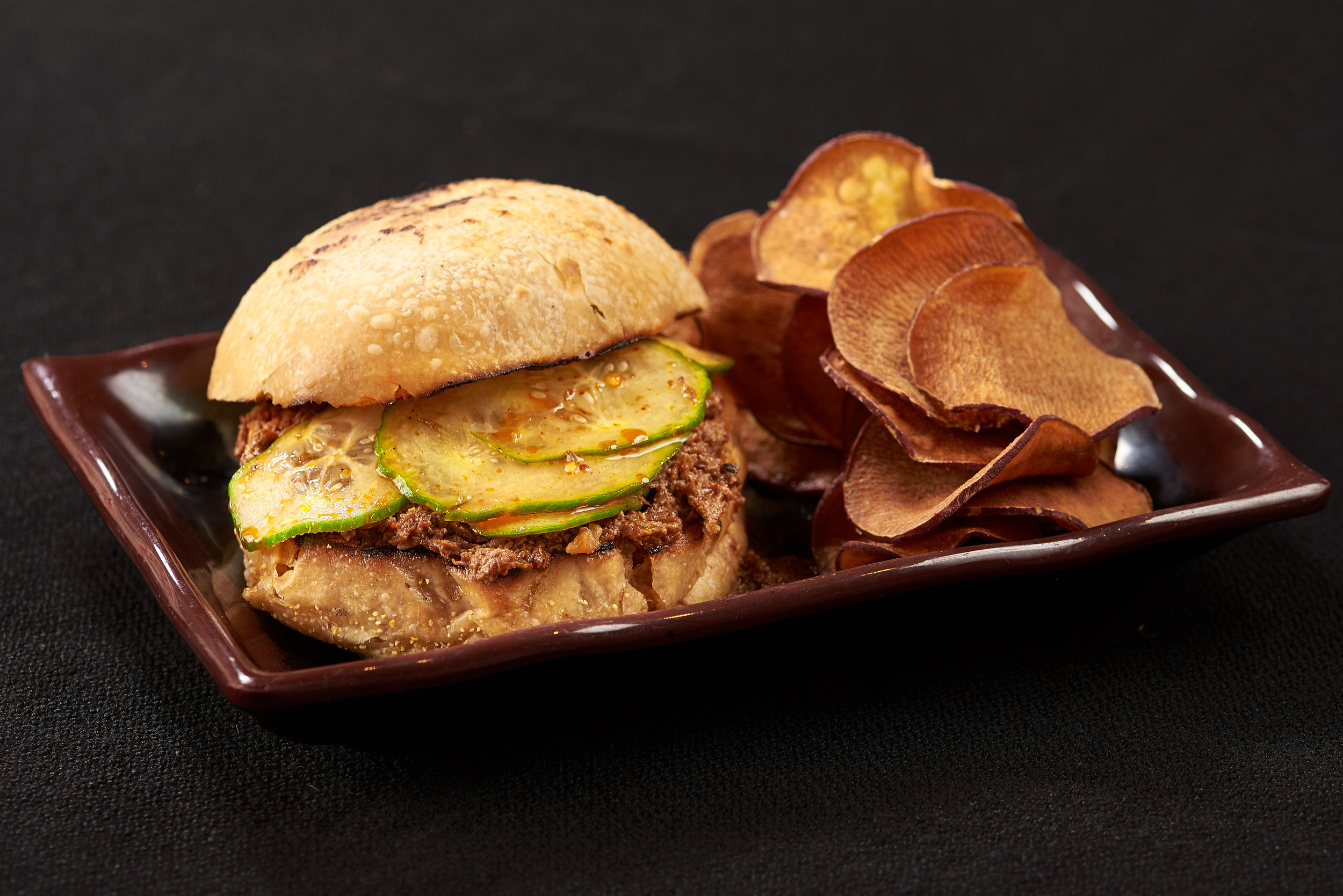 Professional food photo of pulled pork sandwich with pickles and potato chips. Commercial photography
