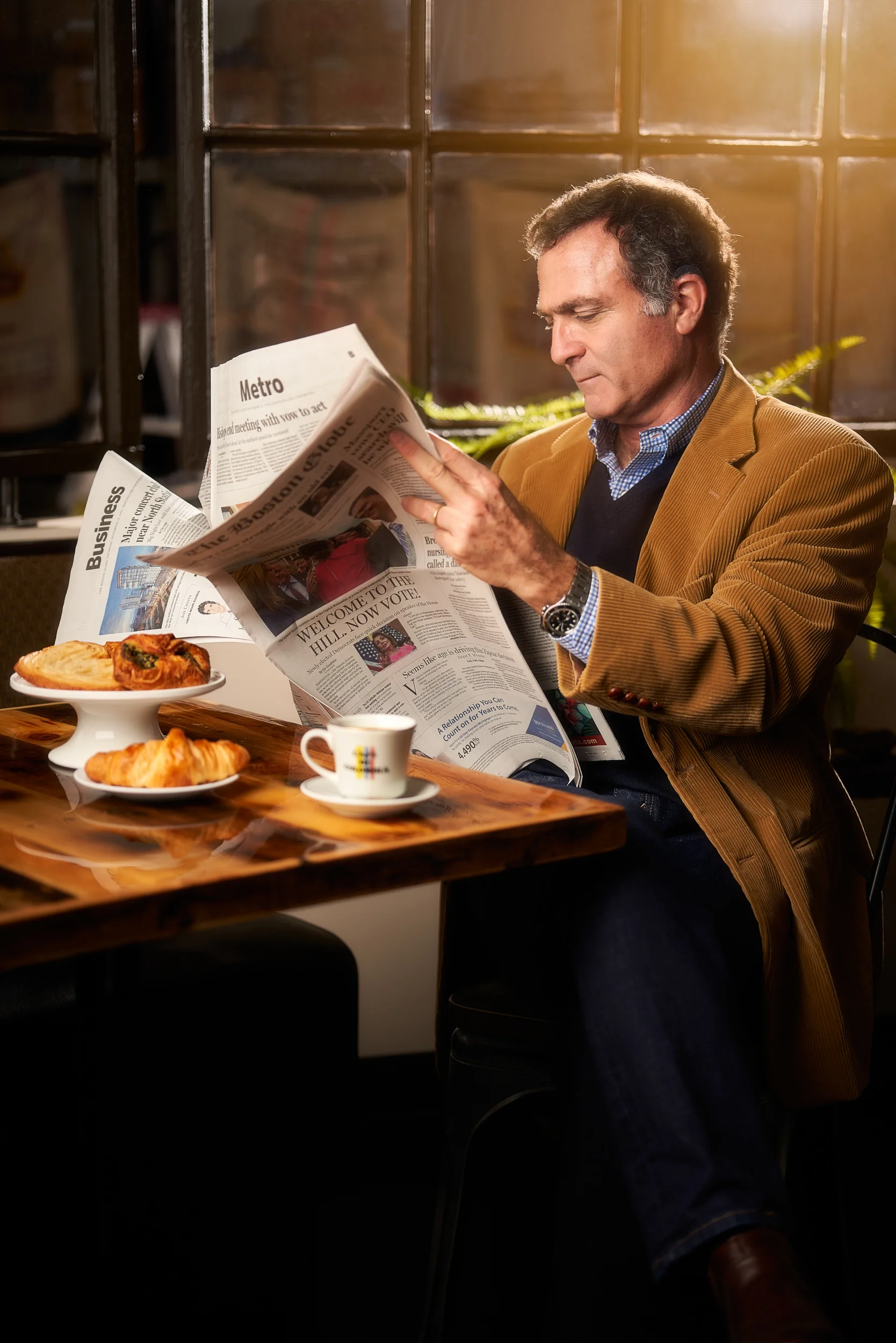 Professional staged picture of a man having breakfast and reading the news paper. For breakfast he is having coffee, croissant and other pastry