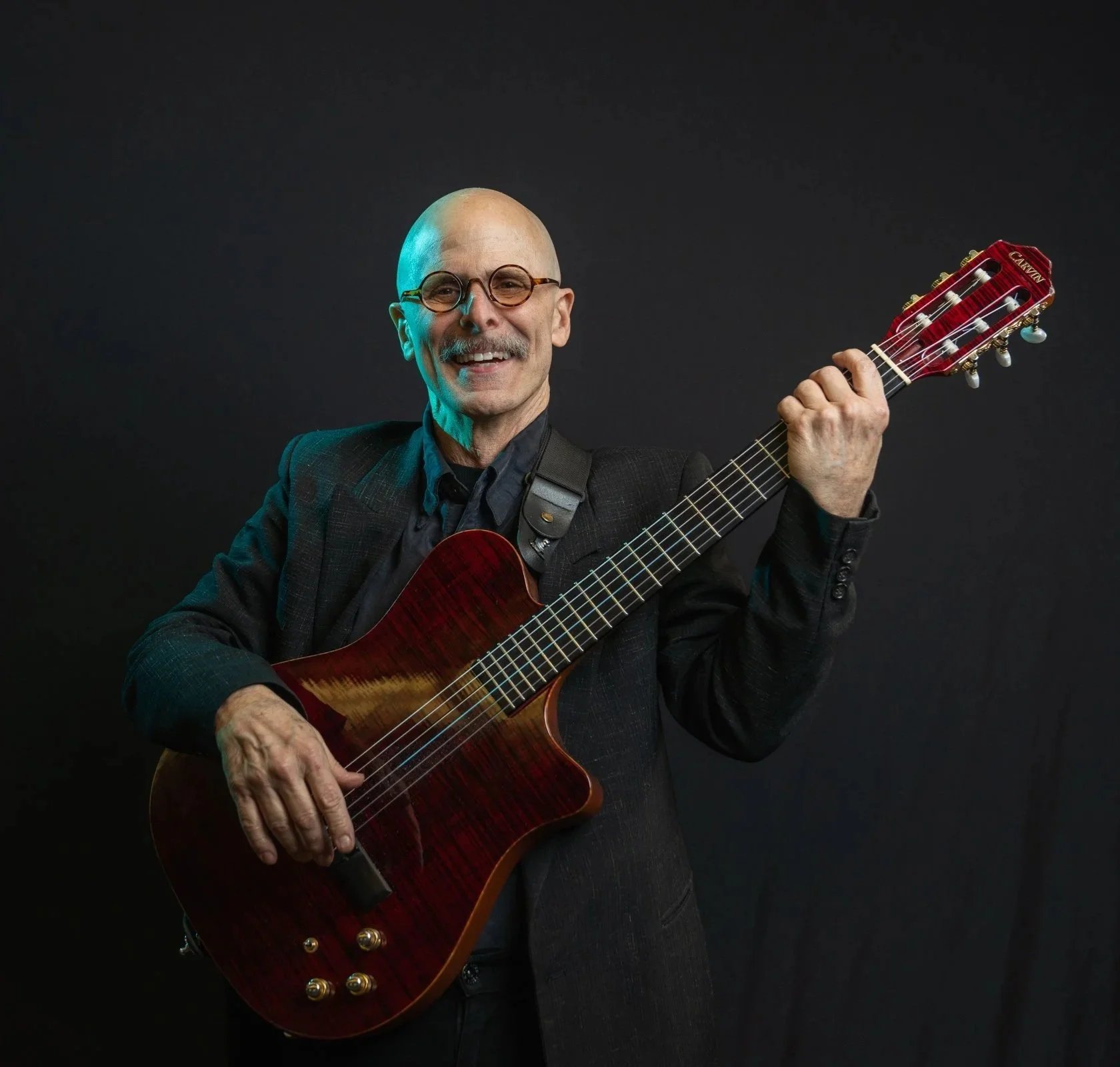 A bald man with a guitar smiles for the camera