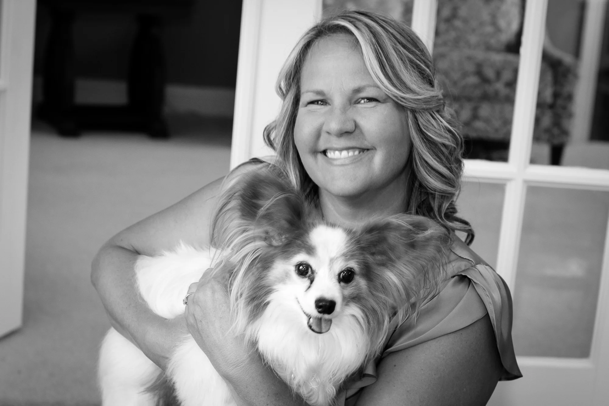A black and white photo of Patricia Keith smiling and holding a dog.