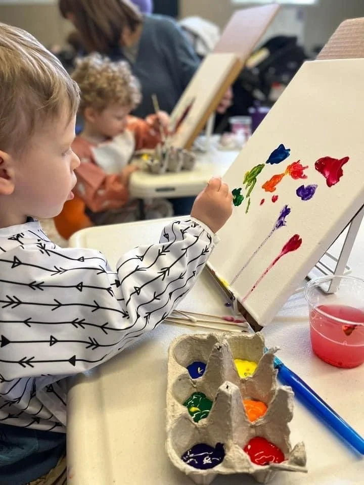 A child paints on a canvas using brightly colored paint.