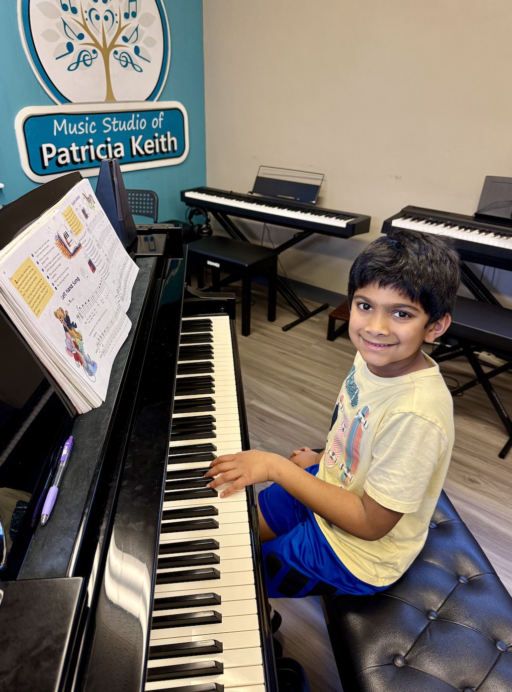 A student sits at a grand piano with his hands on the keys, learning technique at the Music Studio of Patricia Keith.