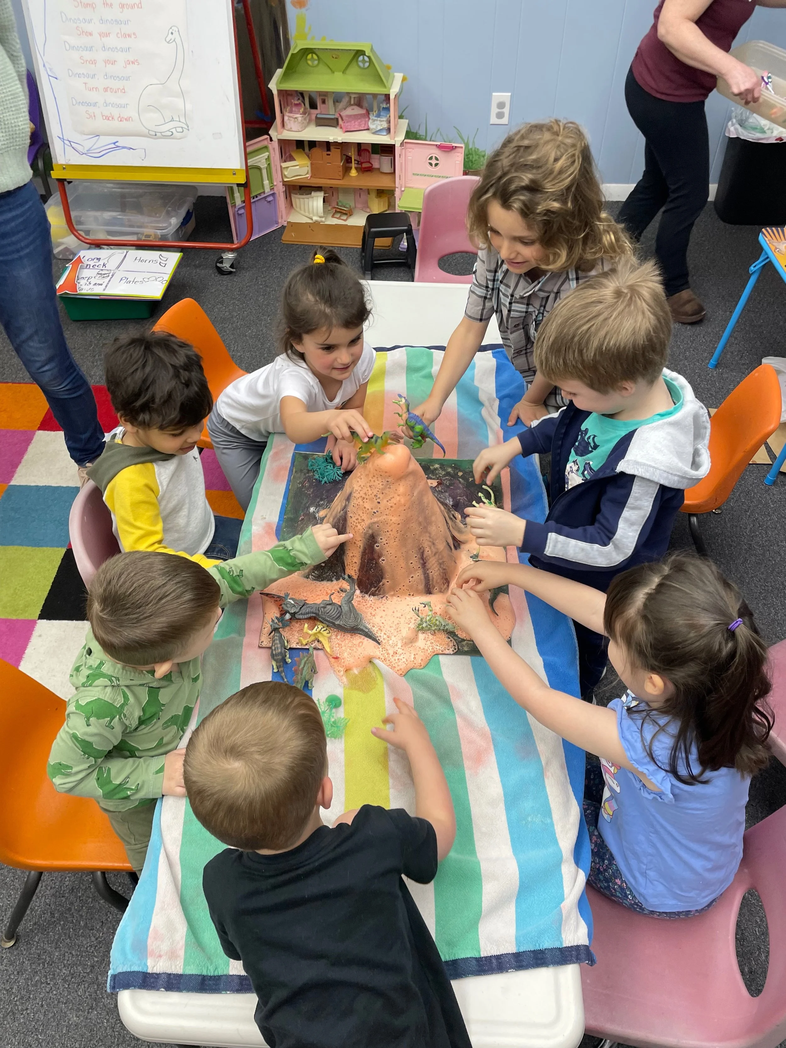 Children gather excitedly around a model of a volcano erupting with a safe chemical reaction.