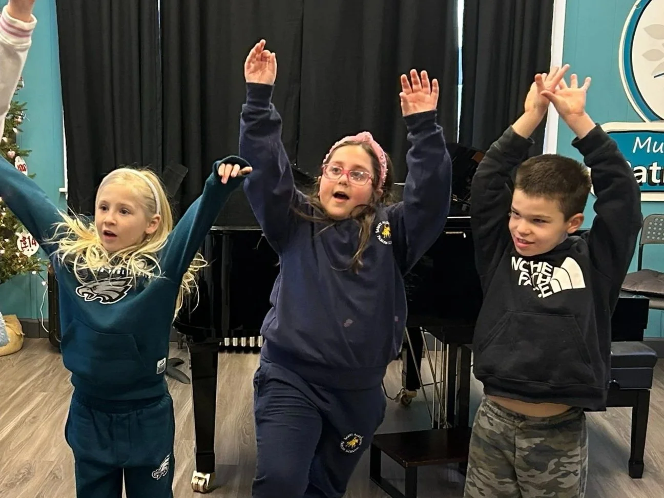 Students raise both their hands high in the air during class at the Music Studio of Patricia Keith