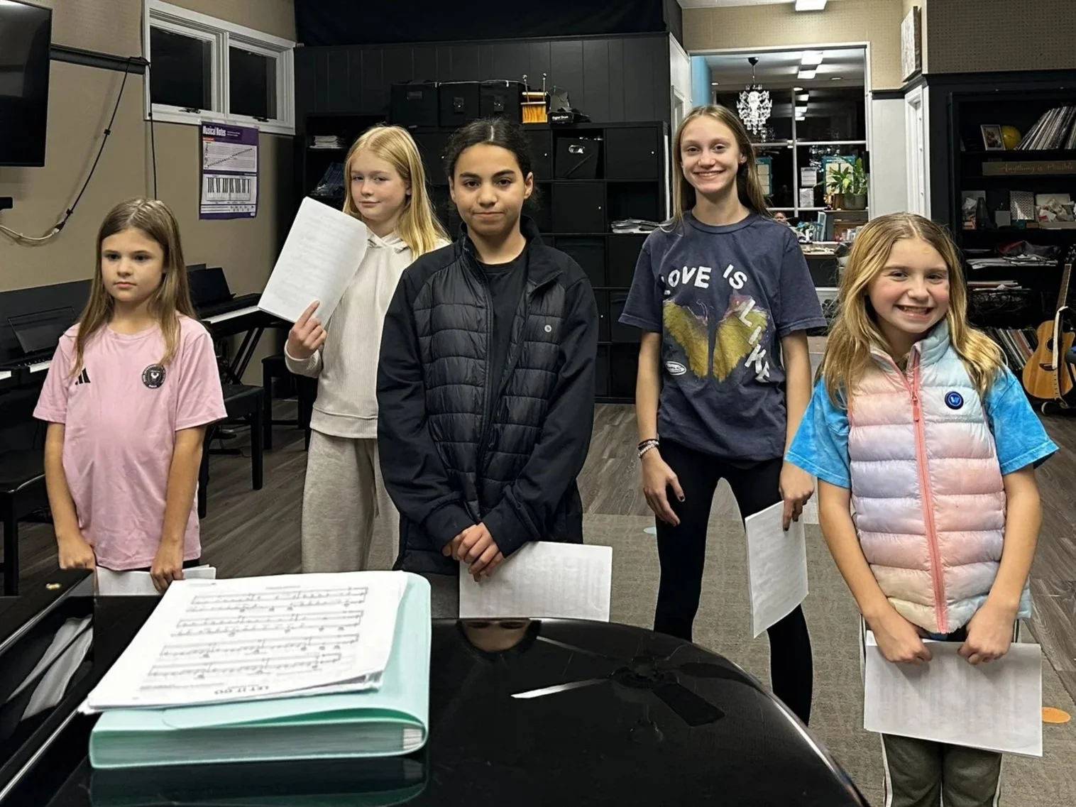 A small group of students is gathered around a piano with sheet music in their performance formation.
