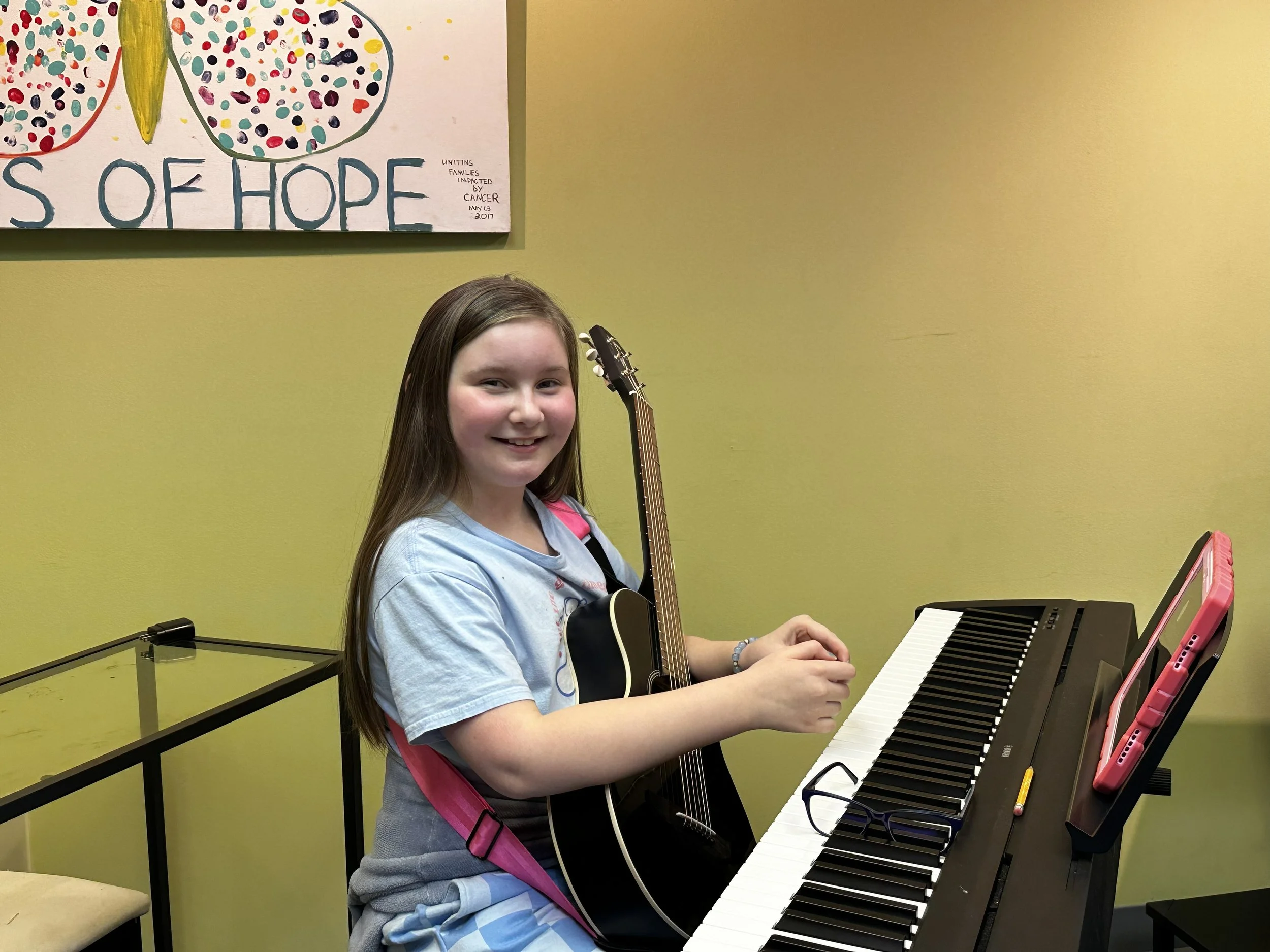 A student with a guitar sitting at a piano keyboard.