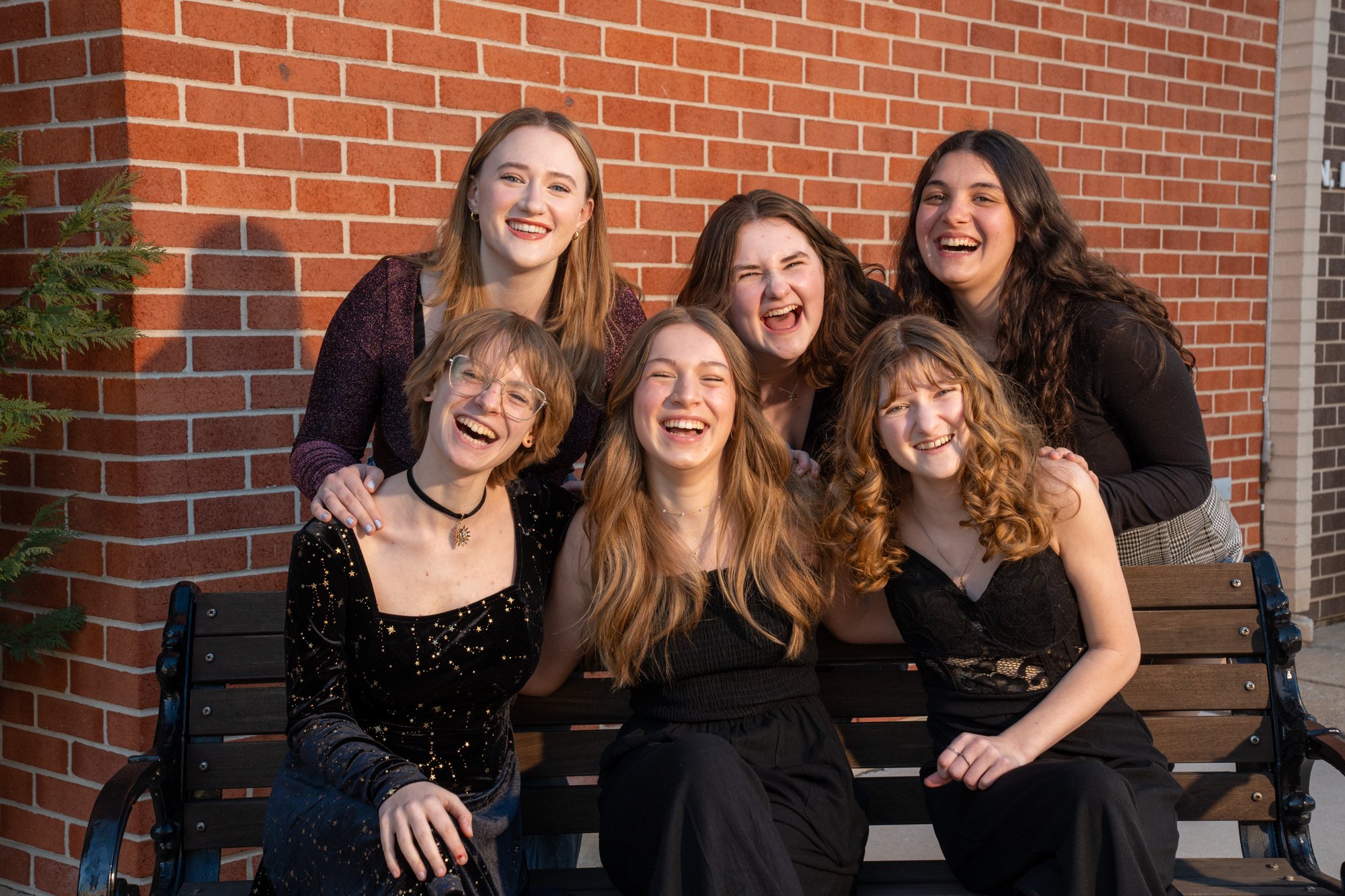 A group of teens in Harmonics a cappella class sitting/standing by a park bench and smiling