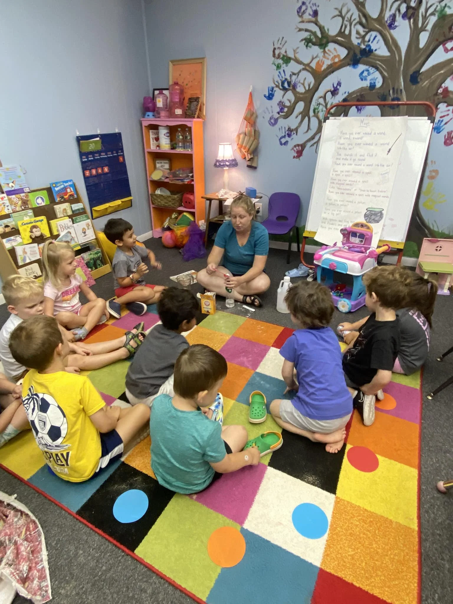 A group of students sits with their teacher on the floor as the teacher shares a science experiment.