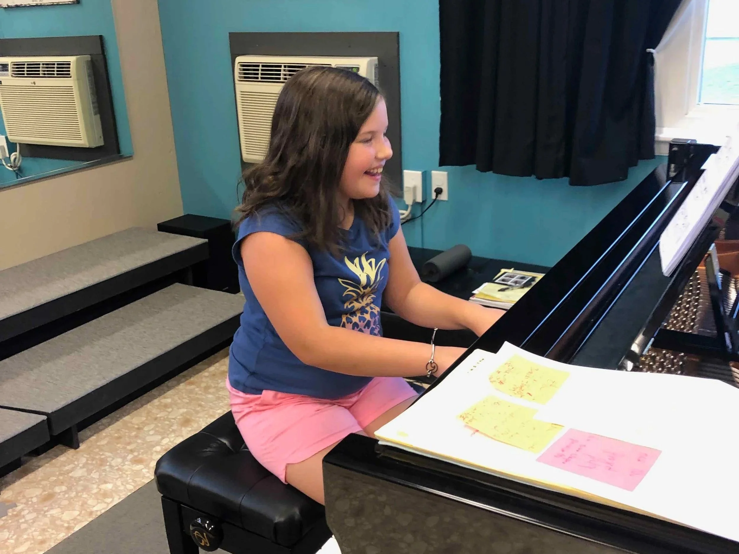 A happy student performs at a grand piano during piano class at the Music Studio of Patricia Keith
