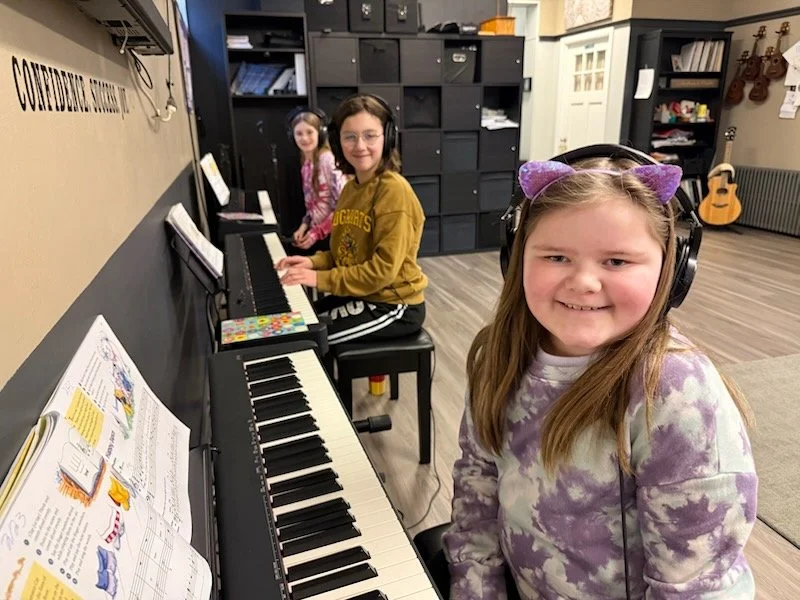Students wearing headphones are seated at keyboards practising during a piano class at the Music Studio of Patricia Keith