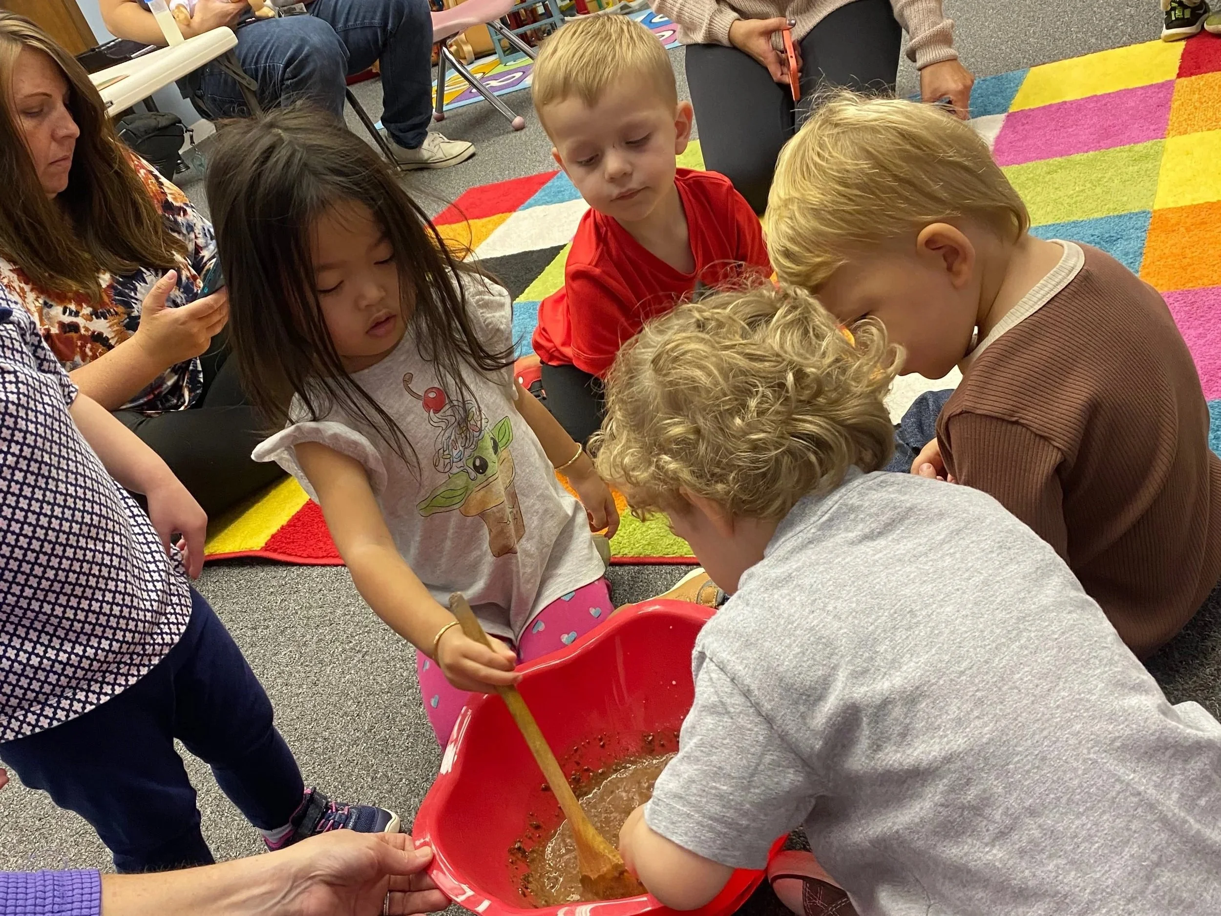 Children gather around a bucket to see what's inside during a science experiment in Early Learning class.