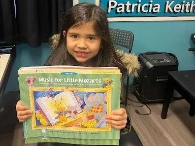 A girl holds up her piano lesson book proudly.