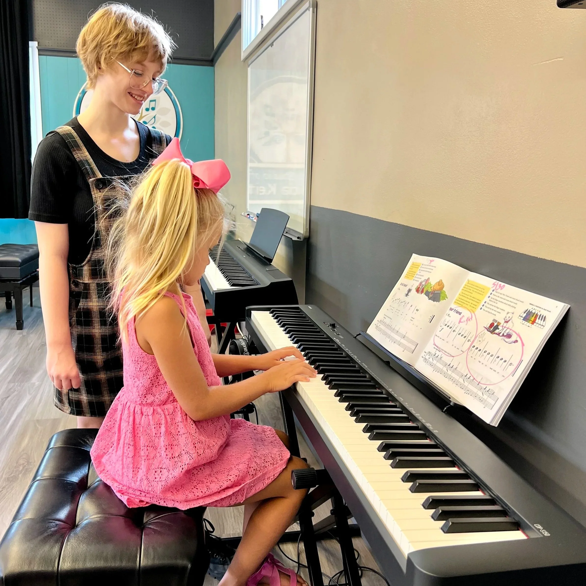 An apprentice teacher directs a student at the keyboard during a piano lesson