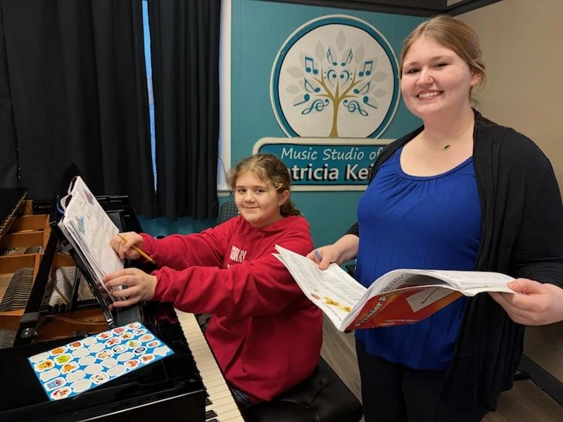 A student looks at her piano book while a class assistant marks pages during piano class at the Music Studio of Patricia Keith in Boyertown PA.