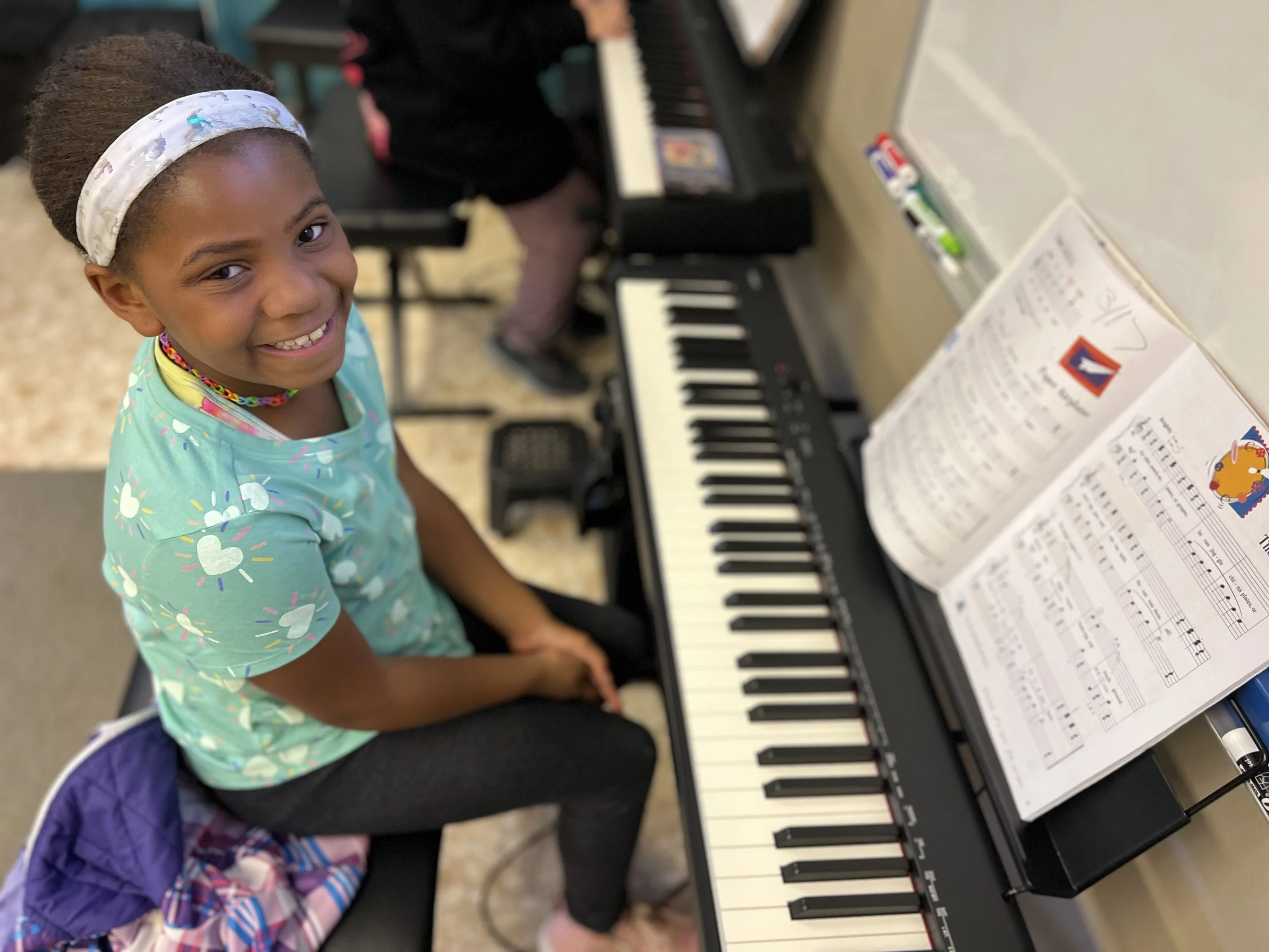 A smiling student looks up from her keyboard during her premier piano class at the Music Studio of Patricia Keith in Boyertown PA