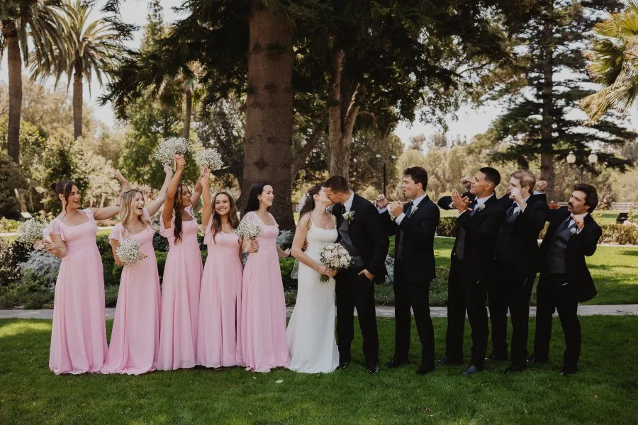 Bride and groom kissing with their wedding party smiling and  cheering