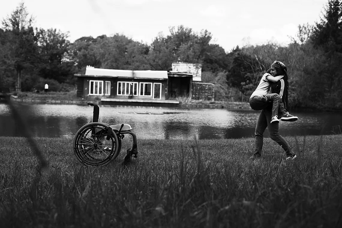 Gena's mom, Sue, carries Gena back to her chair after having her picture taken in a patch of springtime flowers. "She's just so strong, physically and mentally, says Gena. "Numerous years of lifting me and carrying me and pushing a wheelchair throug