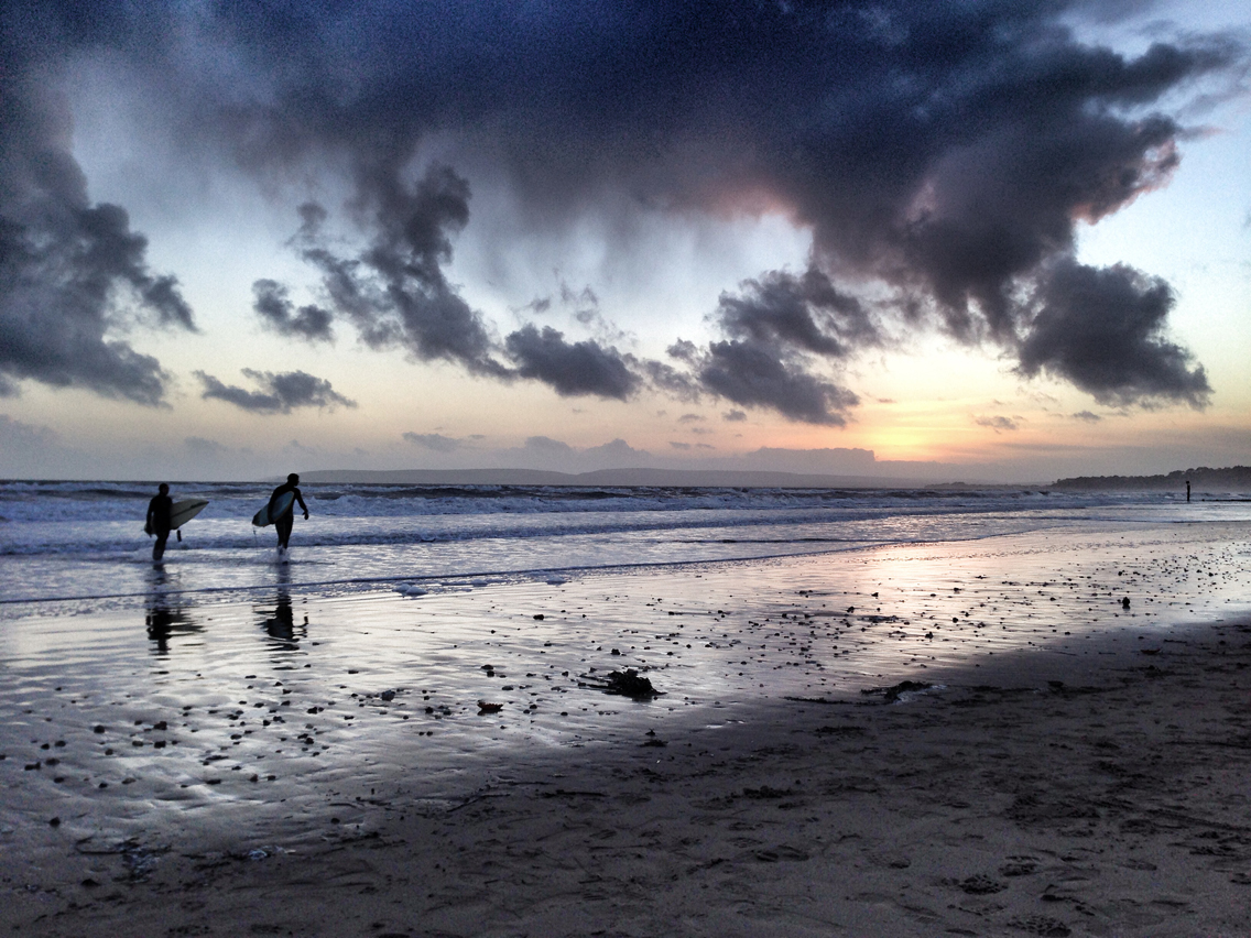 The landscape format illustrates the sheer scale of the beach without overpowering the surfers with too much sand and sky.
