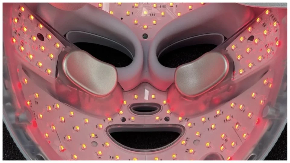 Close-up of a facial mask with LED lights, resembling a smiling face, with eye and mouth cut-outs.