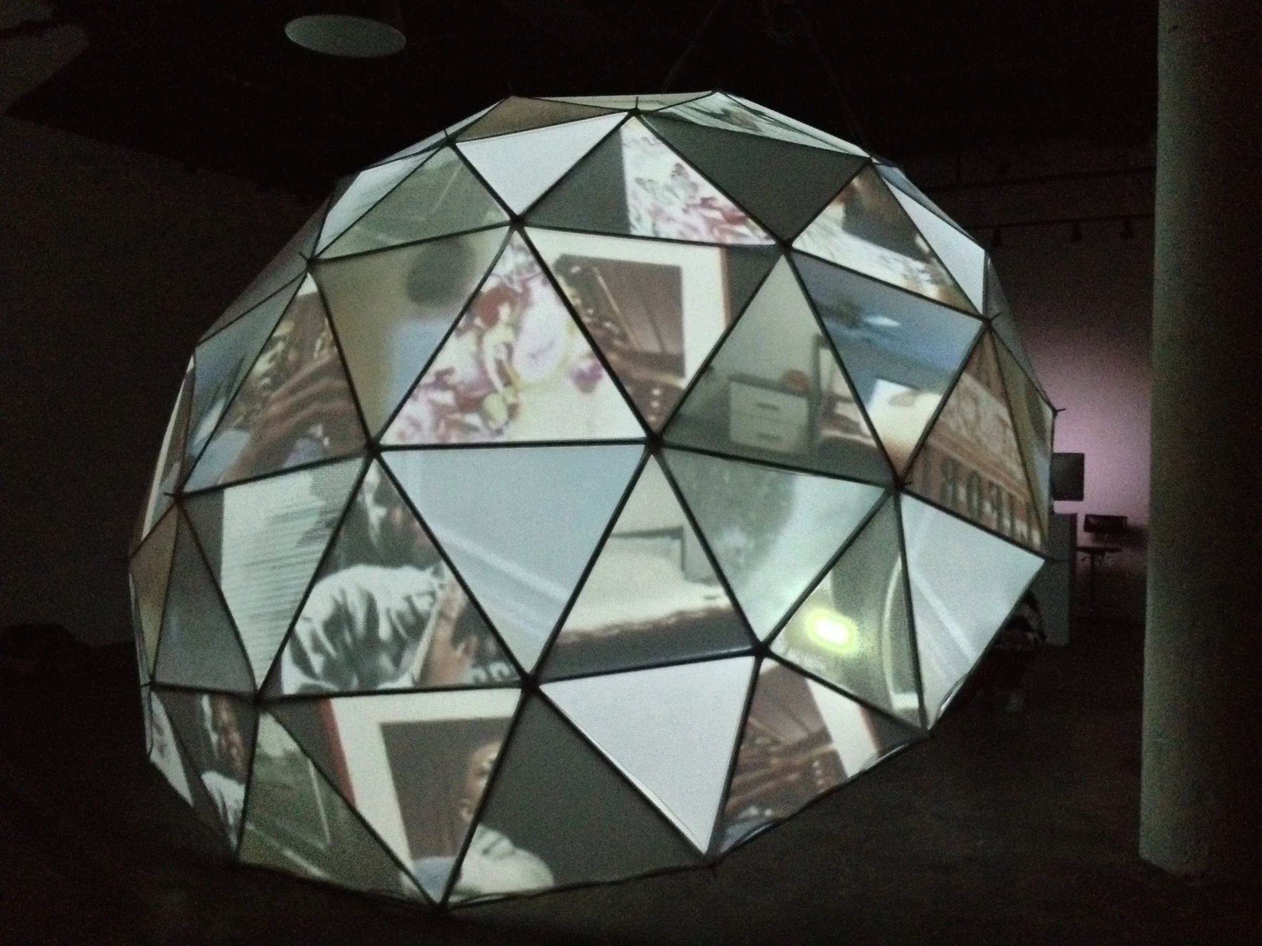 A geometric, faceted, dome-shaped object with reflective surfaces displaying a distorted reflection of a computer monitor with colorful images and a keyboard.