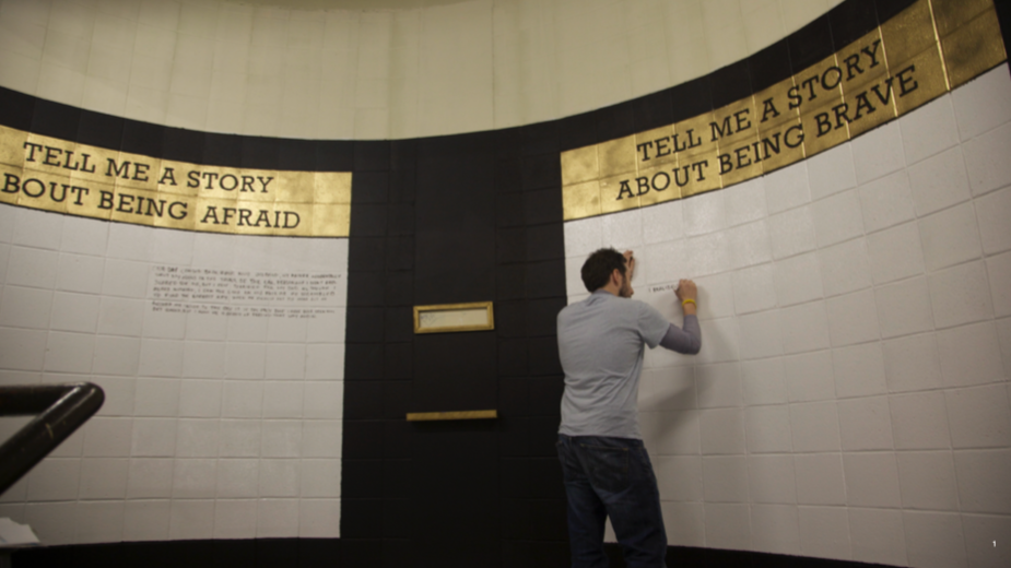 Person writing on a wall with a quote about bravery and fear, surrounded by curved wall with display panels.
