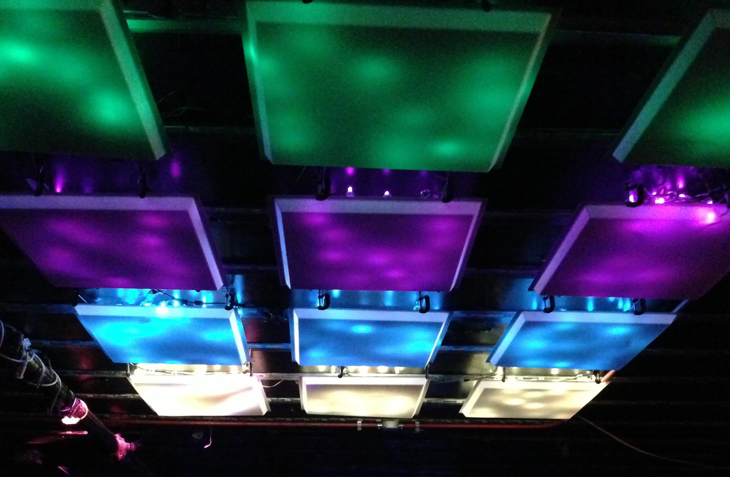 Image of stage lighting with rectangular panels illuminated in green, purple, blue, and white colors.