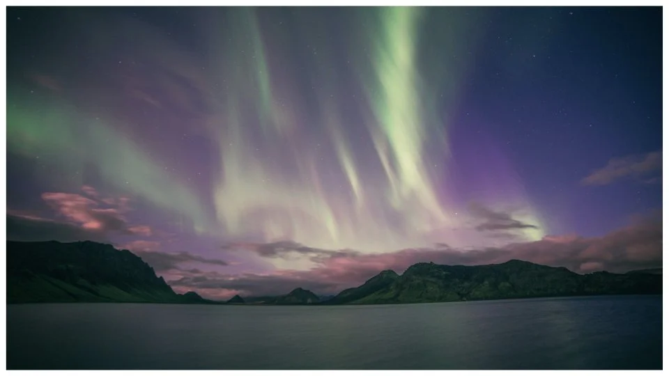 Northern lights over a landscape with mountains and a body of water at night.