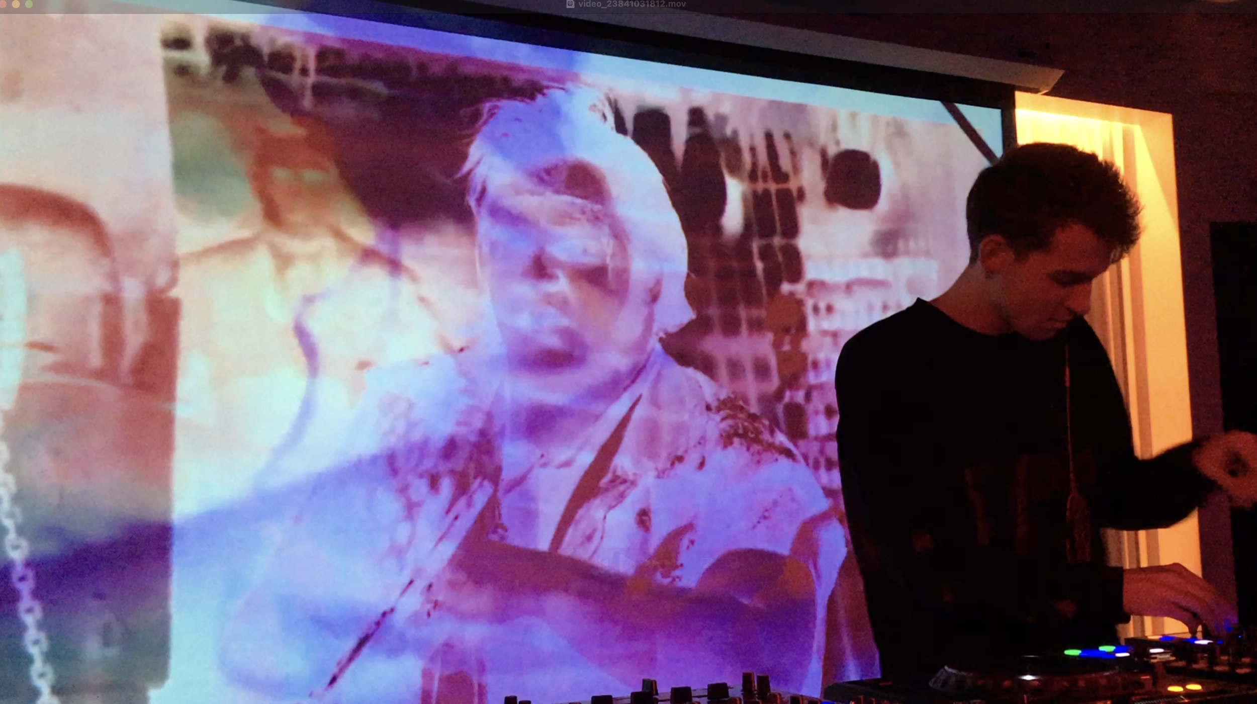 A large projection screen displaying a faded, vintage-style photo of a woman with sunglasses, with people gathered in the background. A person with dark hair, wearing a black shirt, is standing in front of the screen, likely controlling the presentation.