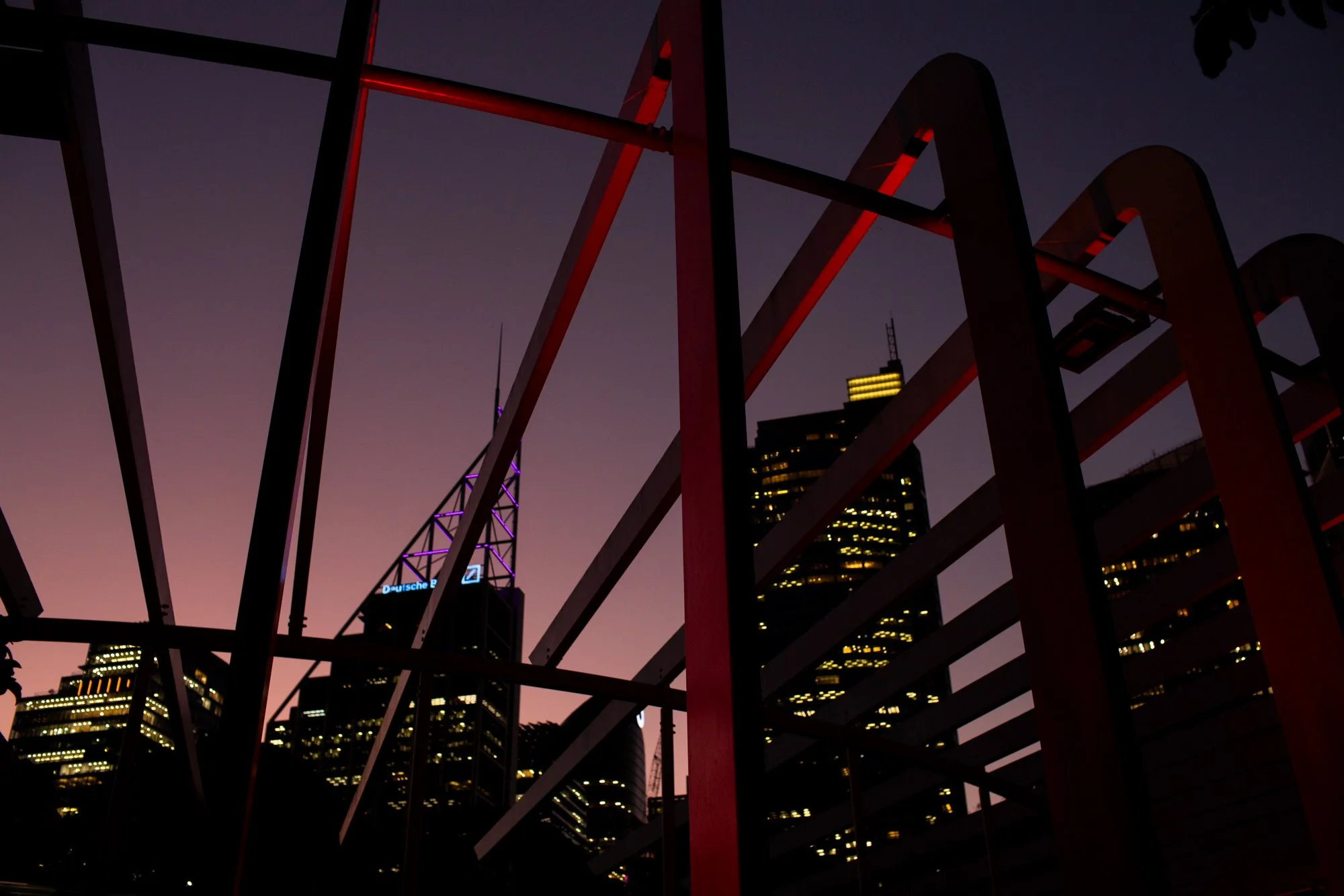 City skyline at dusk with illuminated skyscrapers viewed through a metal railing.