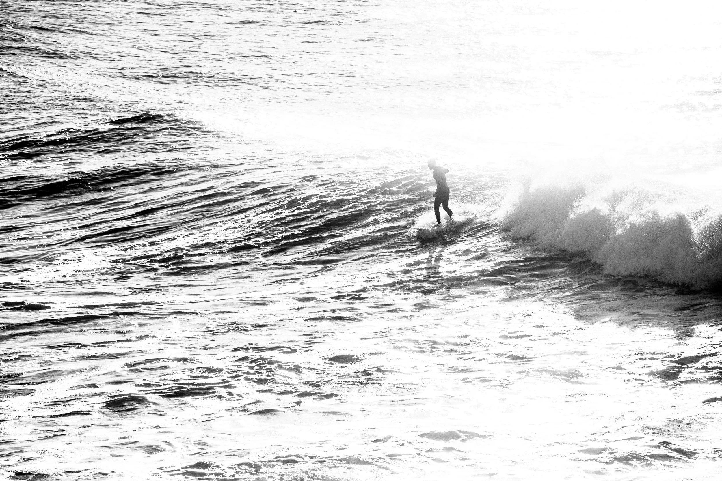A person surfing on a wave in the ocean during sunrise or sunset.