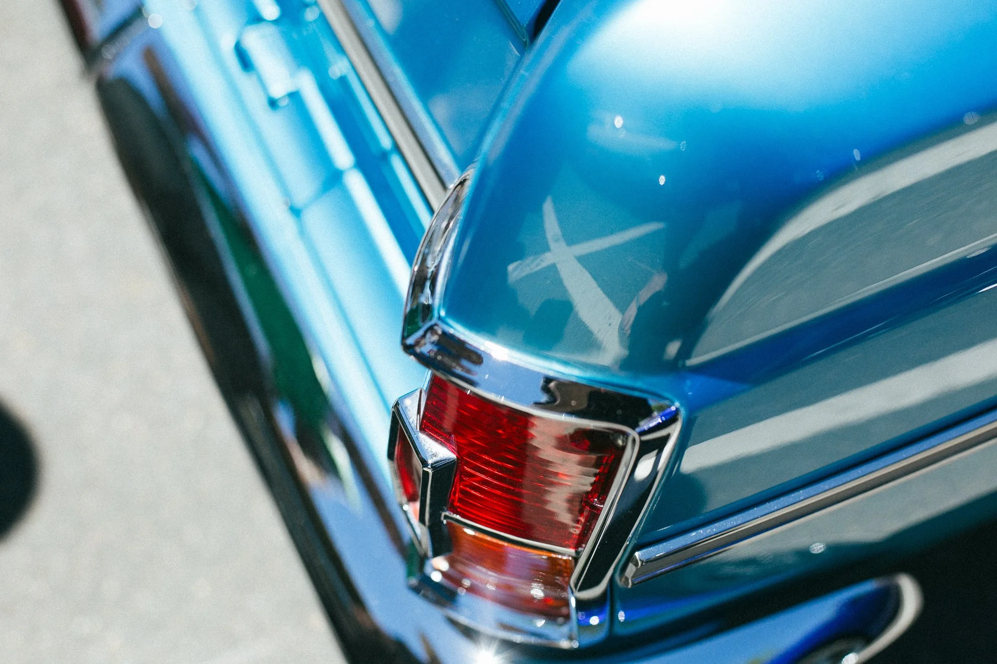 Close-up of the rear corner of a vintage blue car, showing the tail light and chrome details.