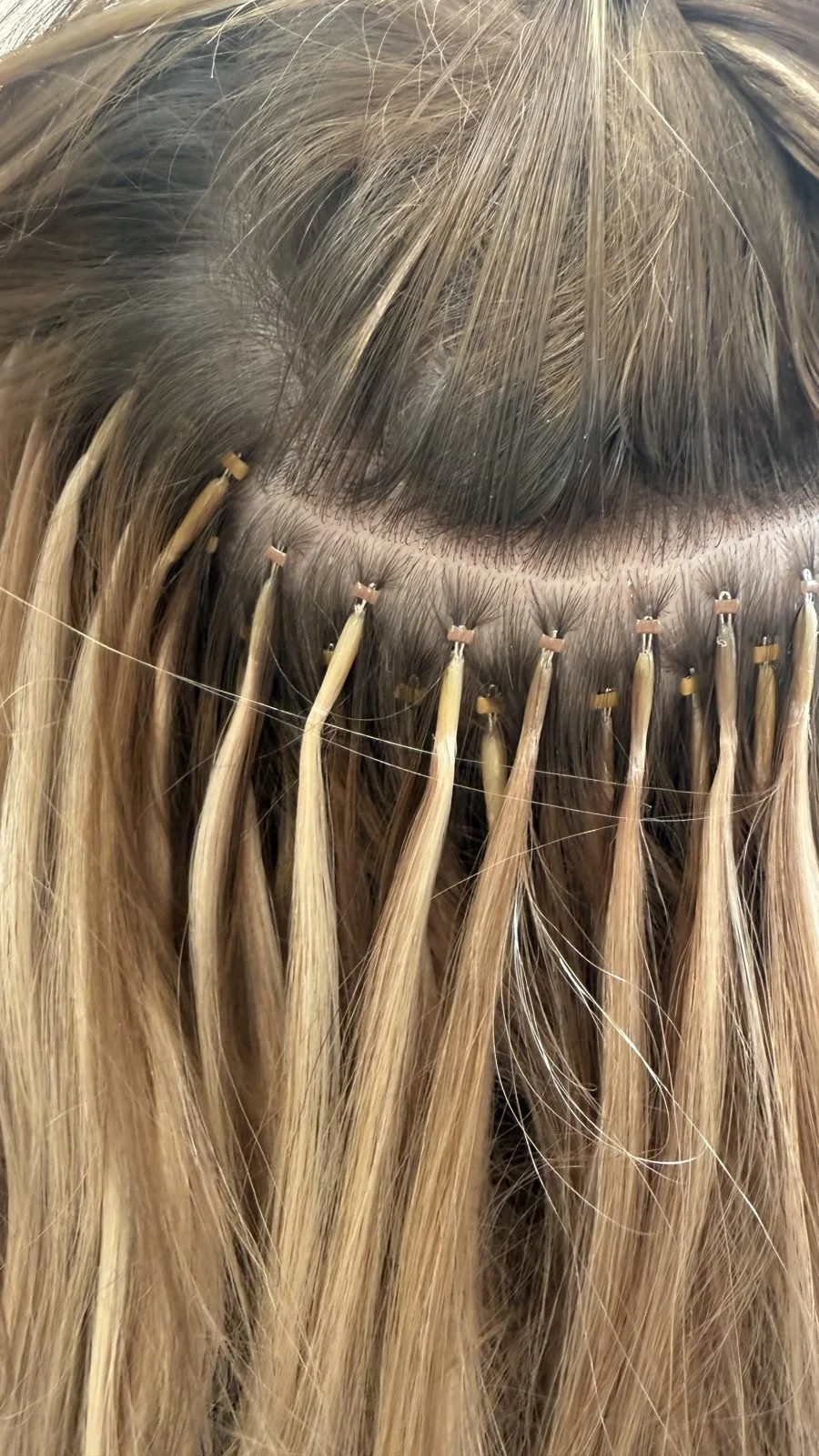 Close-up of microbead extension beads at the root on blonde balayage hair in Boise