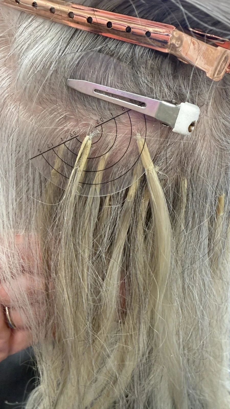 Stylist placing microbead I-tip hair extensions using a sectioning guide on silver blonde hair in Boise