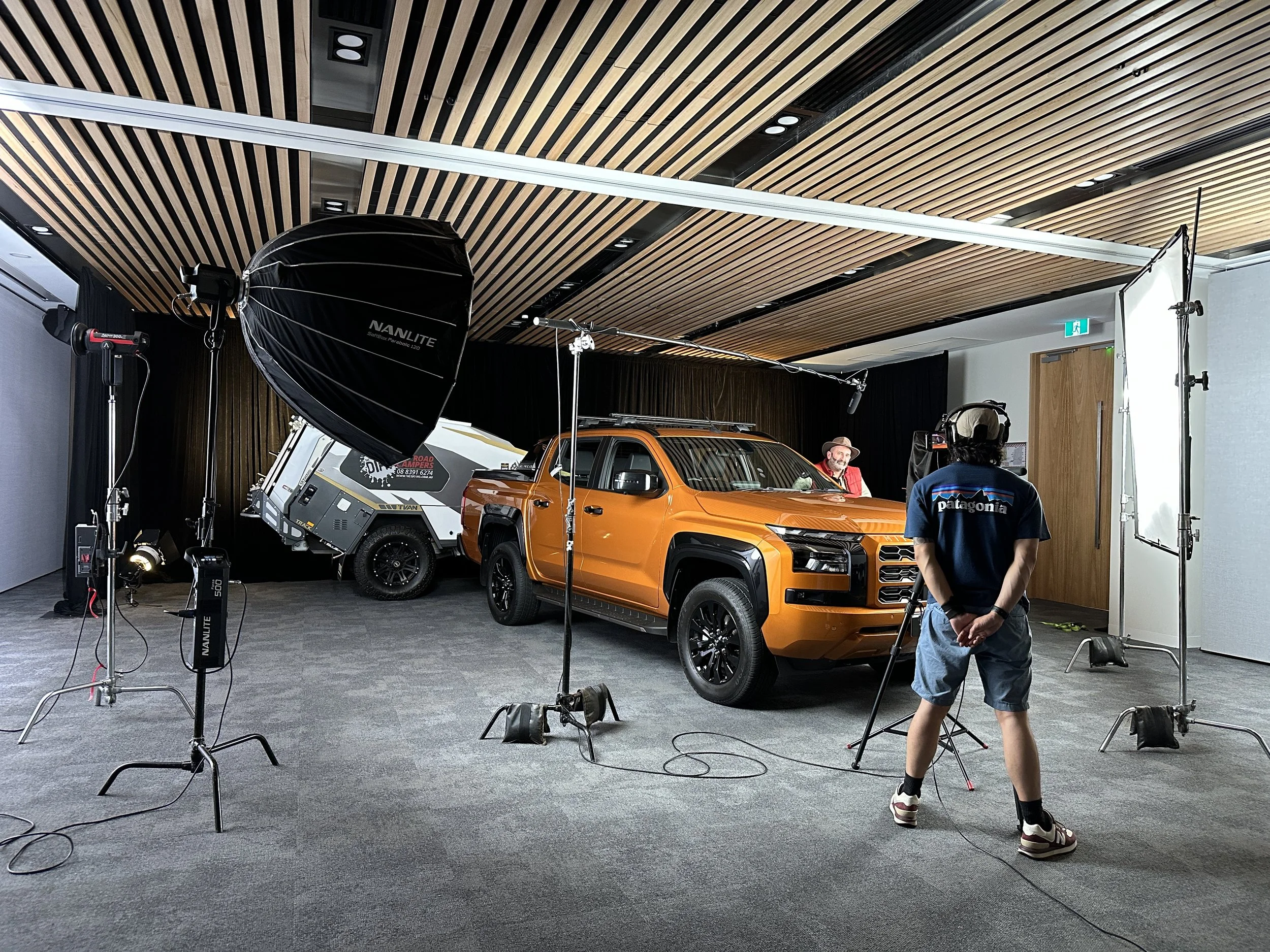 Lights and microphone around Mitsubishi Triton with trailer in the background, with on screen talent talking to camera