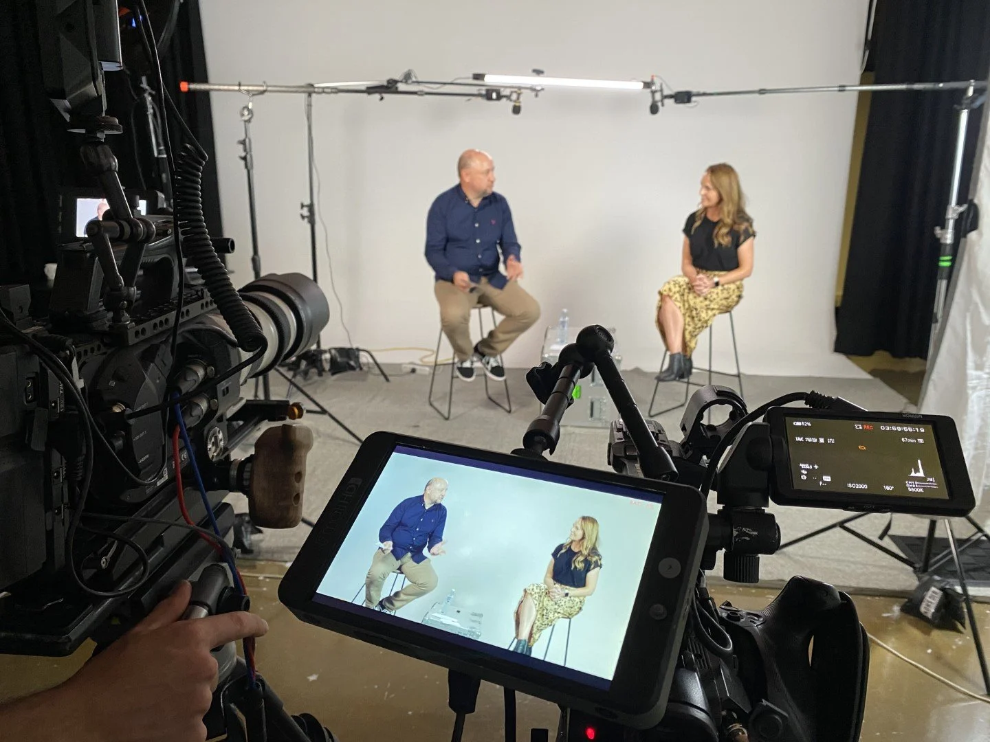 Man and woman sitting on a white cyclorama with camera's filming their conversation