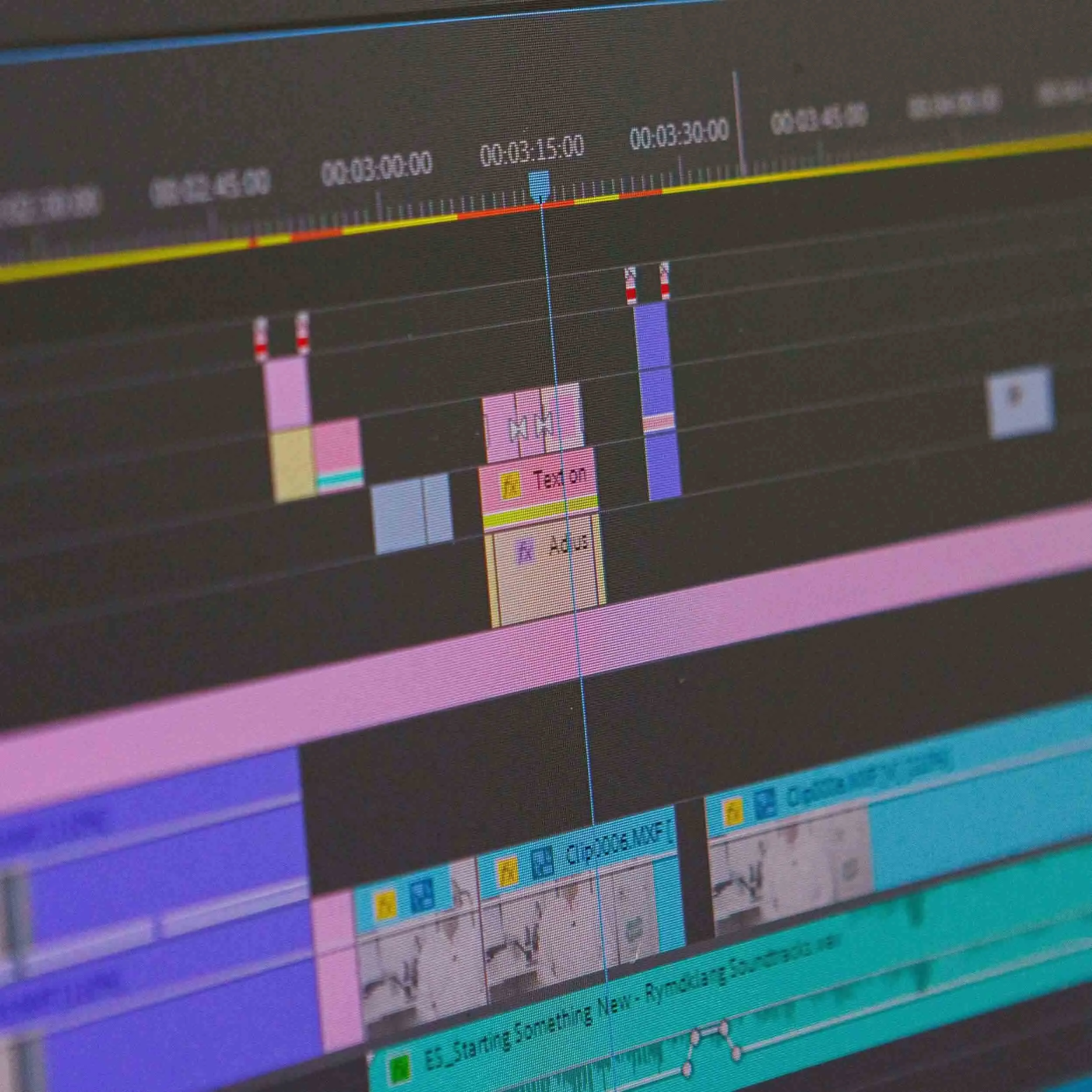 Close-up of a computer screen displaying an editing timeline with various color-coded tracks, video clips, and audio waveforms, including text overlays and editing markers.