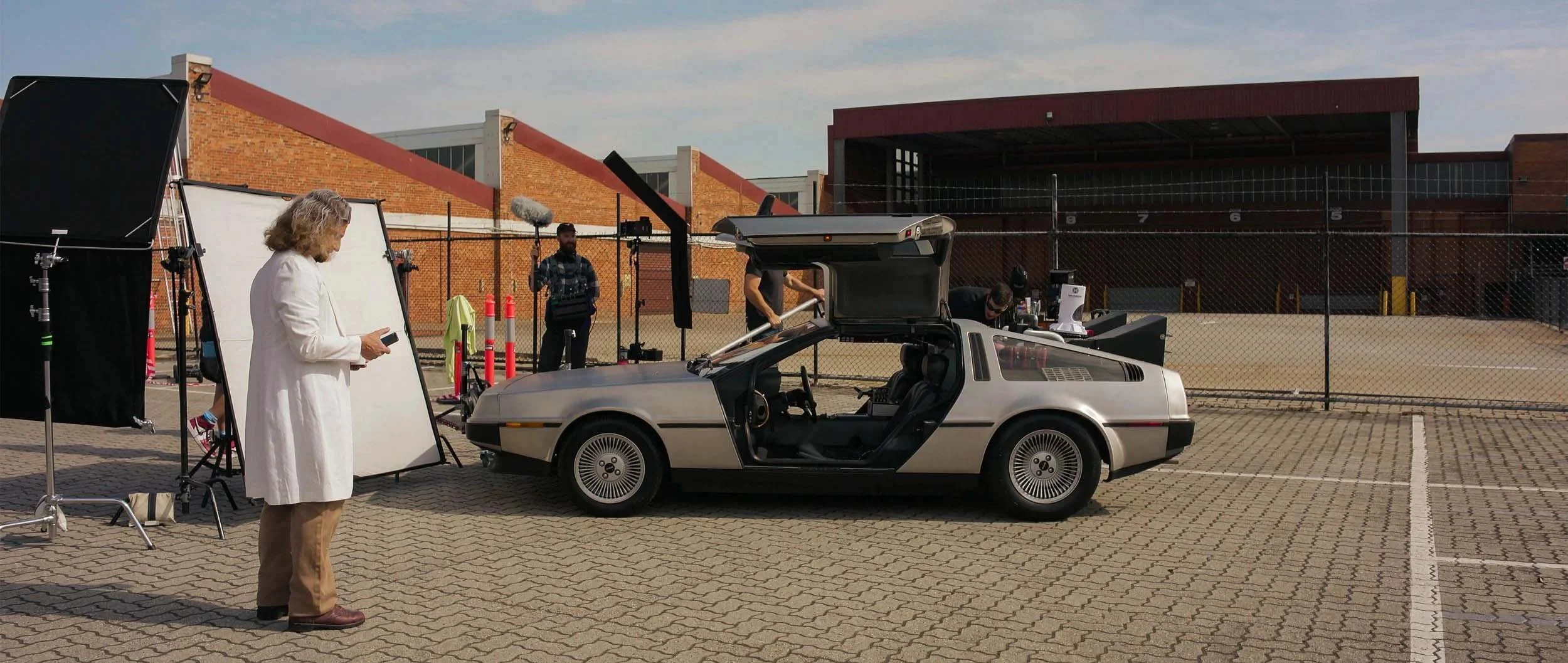 Film crew setting up filming scene with a DeLorean car at an outdoor location.