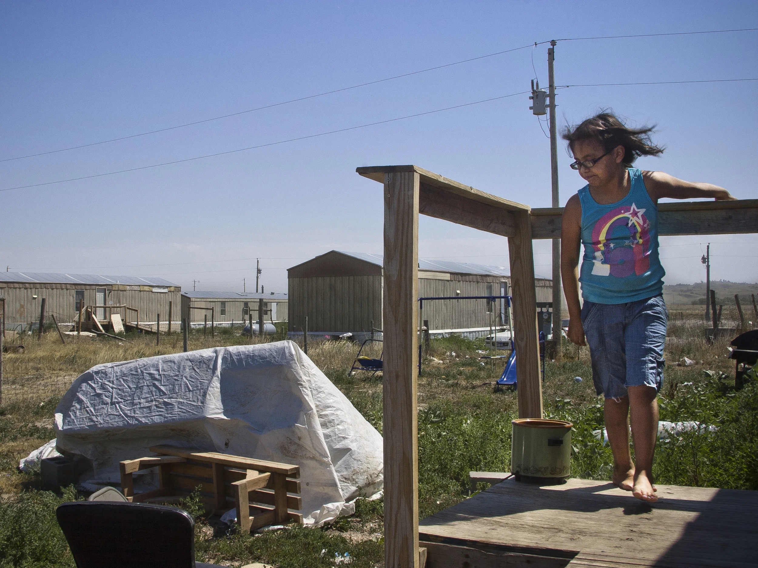 A young Oglala Sioux girl stands on the porch of her home on the Pine Ridge reservation in South Dakota. Tornadoes that devastated the county in the summer of 1999 destroyed over 150 homes, and many still live in the temporary emergency trailers provided by FEMA in the storm's aftermath.