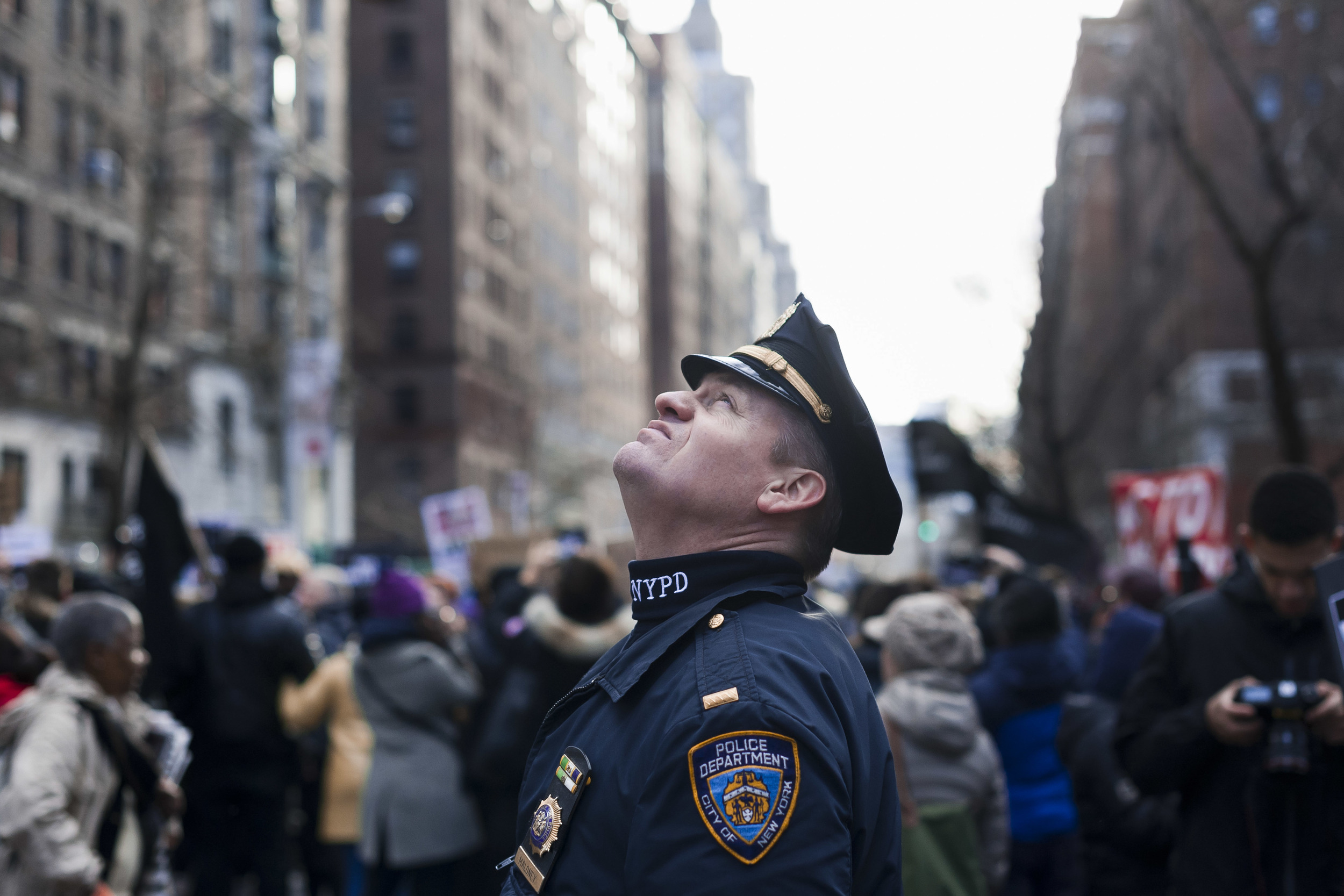  an NYPD officer looks up at the circling news helicopters before a "Millions March" demonstration on December 13th, 2014&nbsp;that drew more than 60,000. 