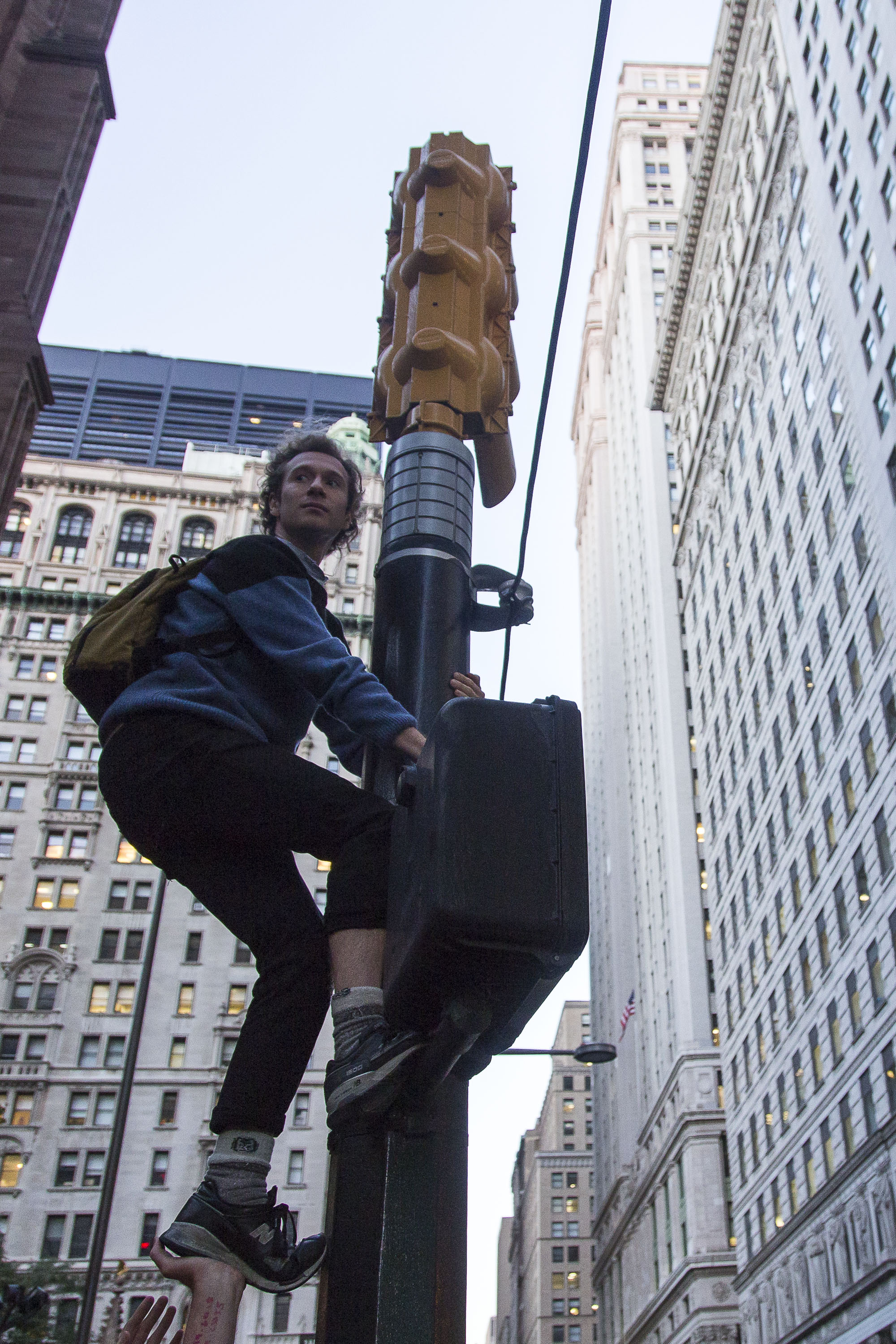Against the wishes of the NYPD, a protestor scales a traffic signal for a better view.