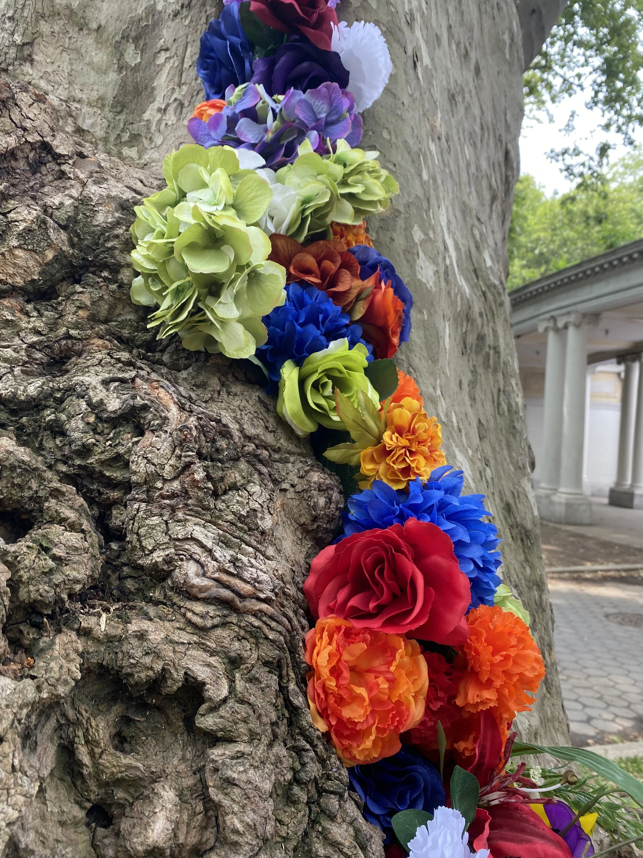 Site-specific installation with styrofoam, silk flowers, living tree, community participation, McGolrick Park, Brooklyn, NY, June 2023.