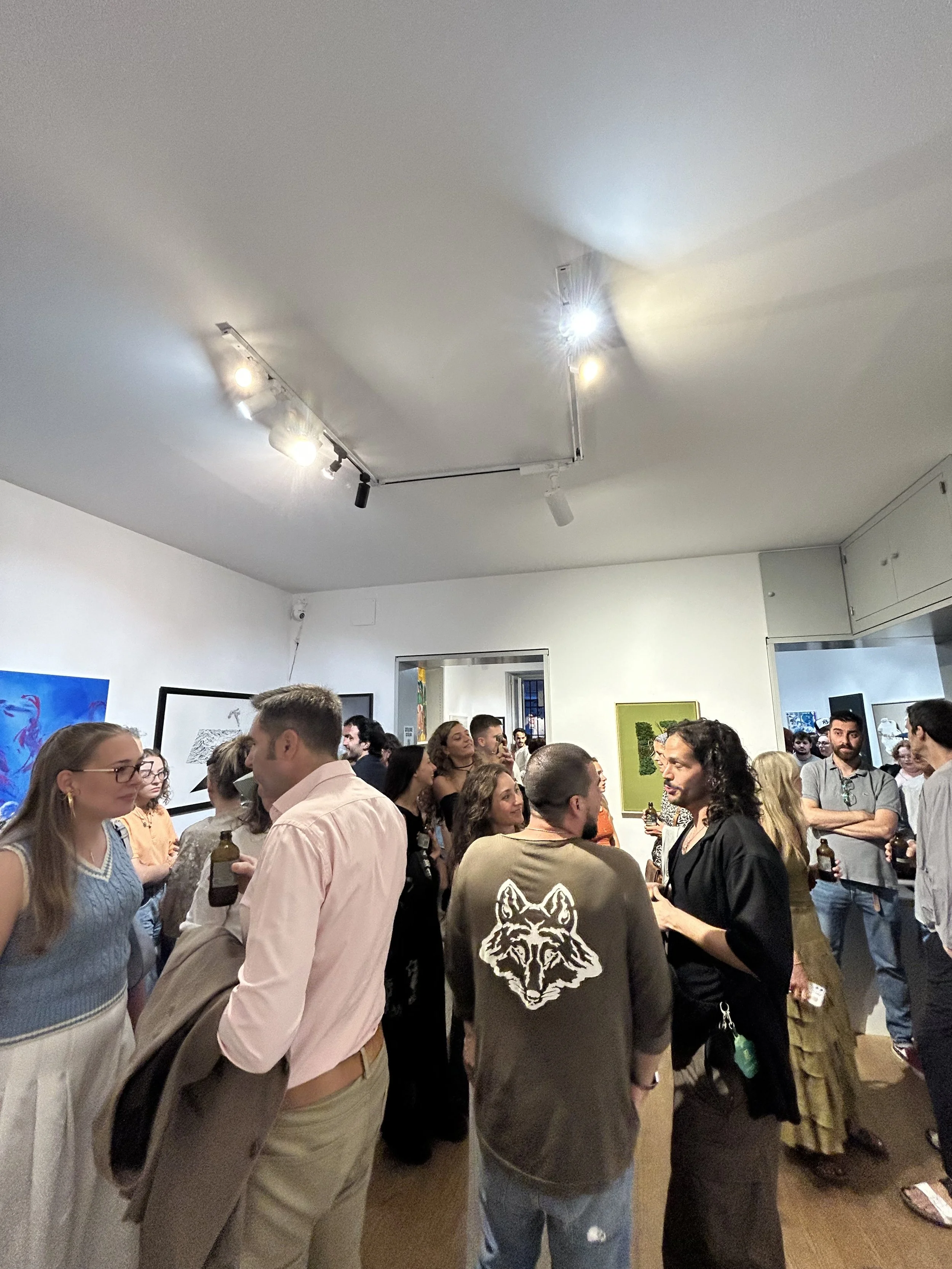 People gathered in an art gallery, engaging in conversations while viewing artwork displayed on the walls.