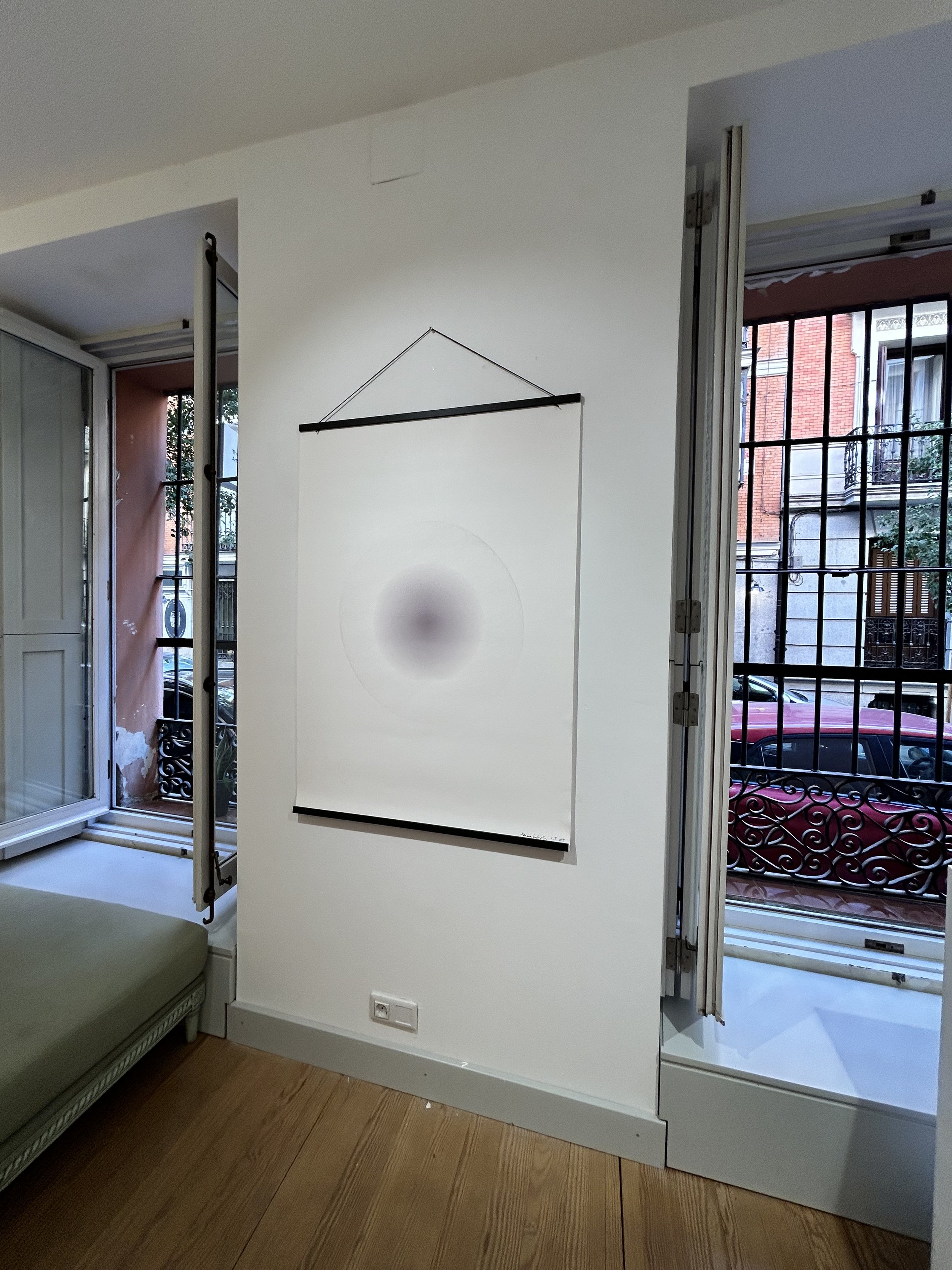 Interior of a room with open windows and a hanging art piece on the wall, showing a blurred circular central pattern.